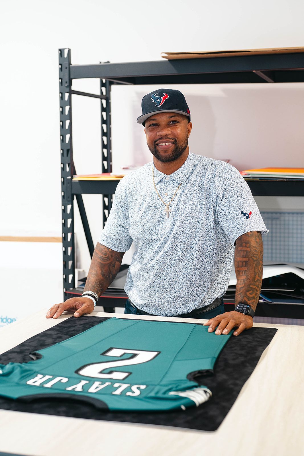 Man standing behind a table, holding up a teal Miami Marlins jersey in a workshop.
