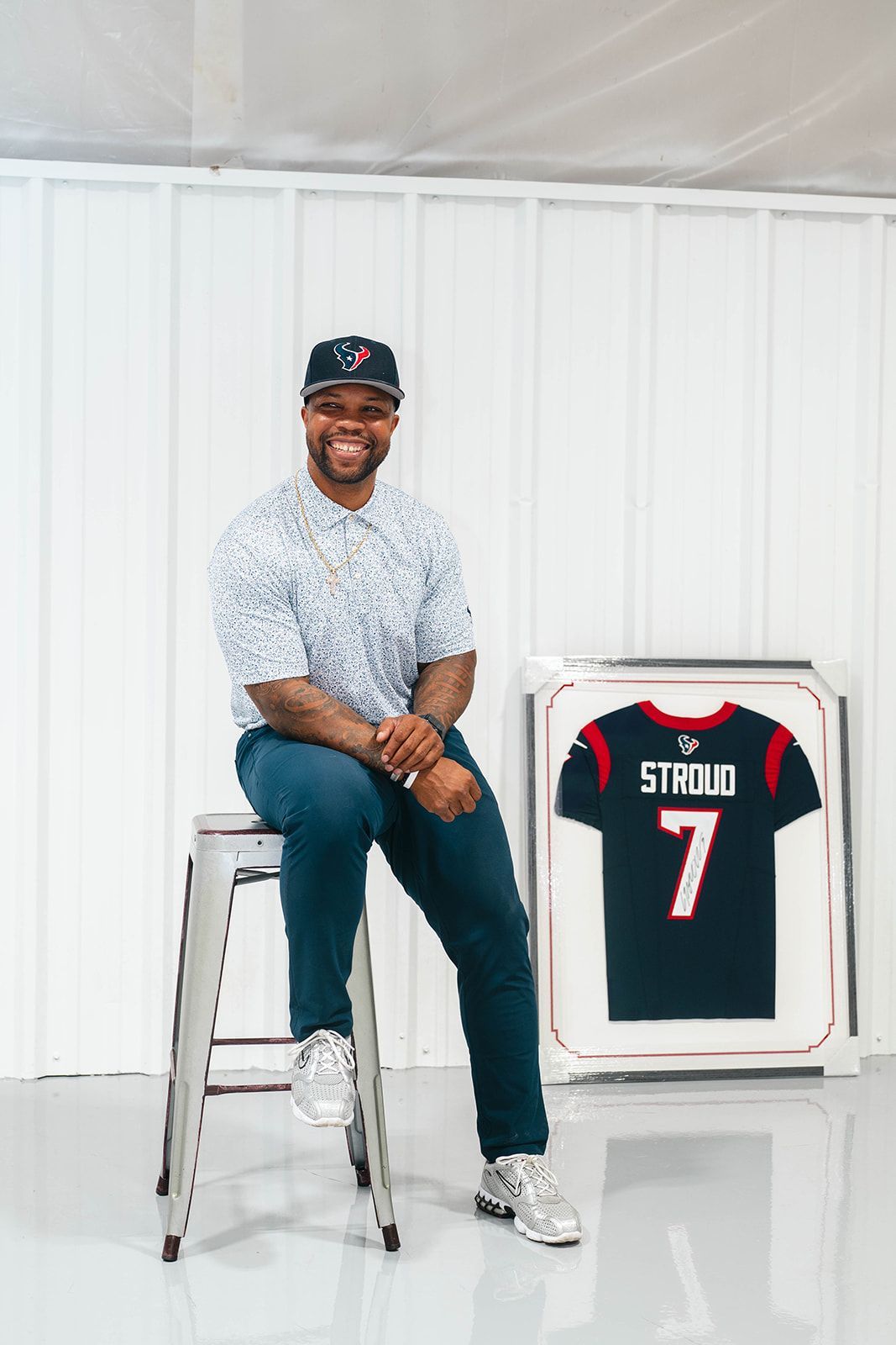 Man seated on a stool beside a framed black football jersey with number 7 in a bright white studio