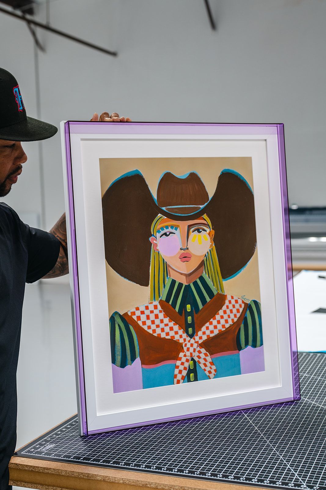 Framed colorful portrait painting on a patterned table, with a person partially visible at left