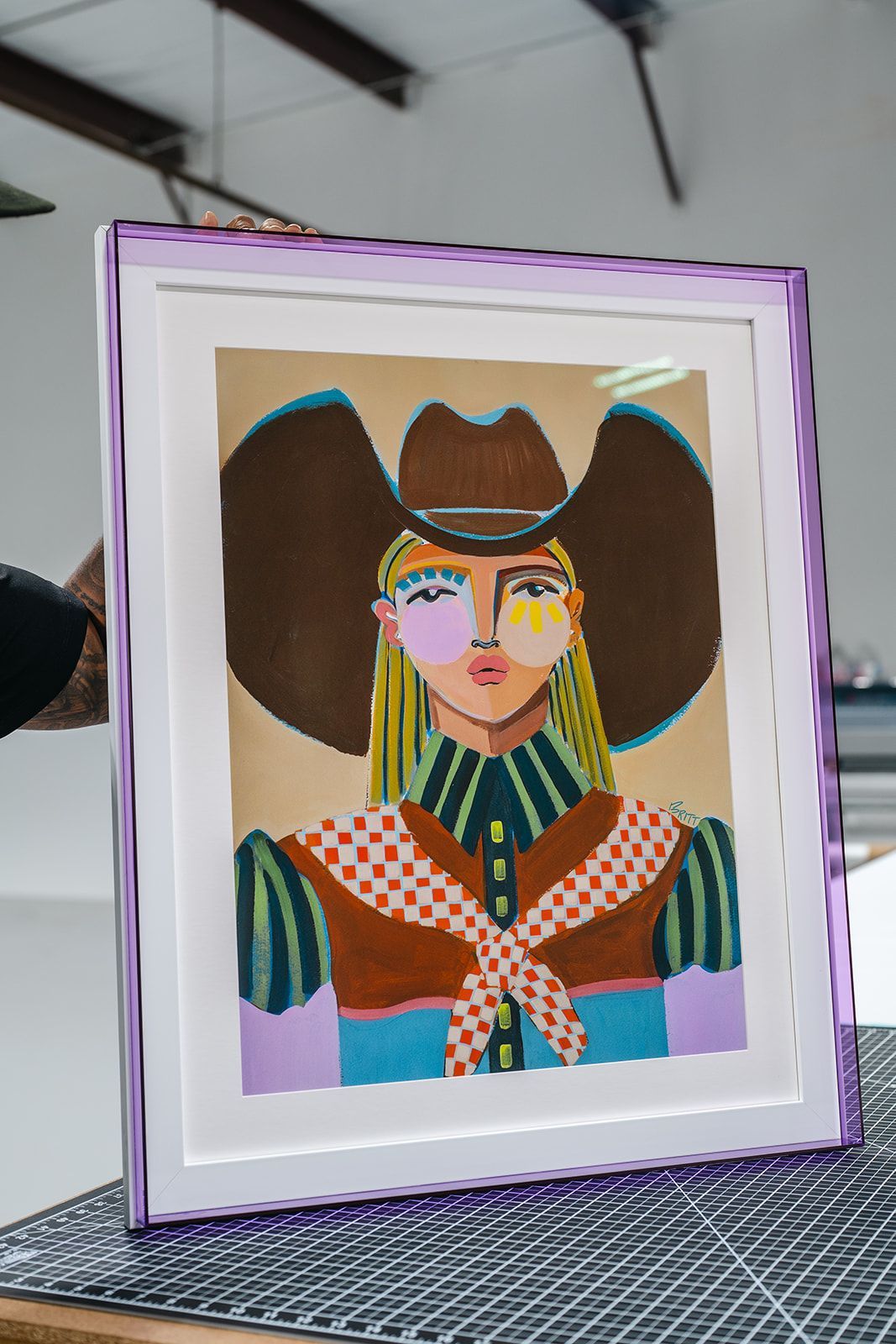 Framed colorful portrait artwork with a stylized face and brown hair on a table.