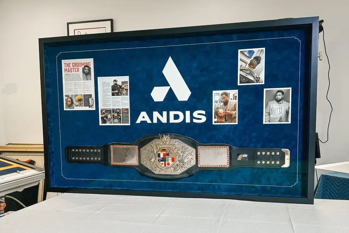 Blue display case with ANDIS logo, four photos, and a championship belt on a white surface