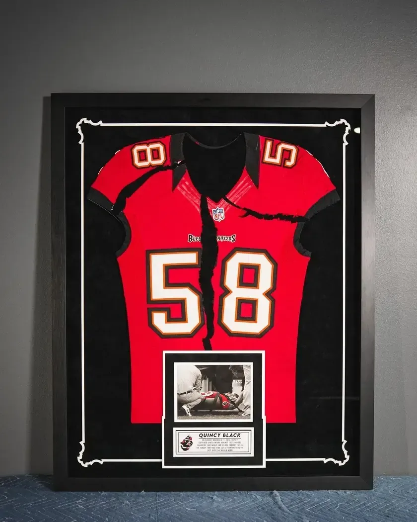Framed red football jersey with number 58 and a small plaque beneath it on a gray wall
