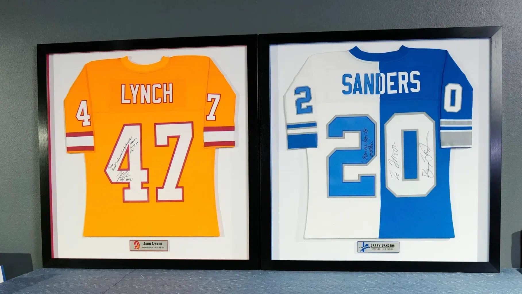 Framed football jerseys of Lynch #47 in orange and Sanders #20 in white and blue side by side