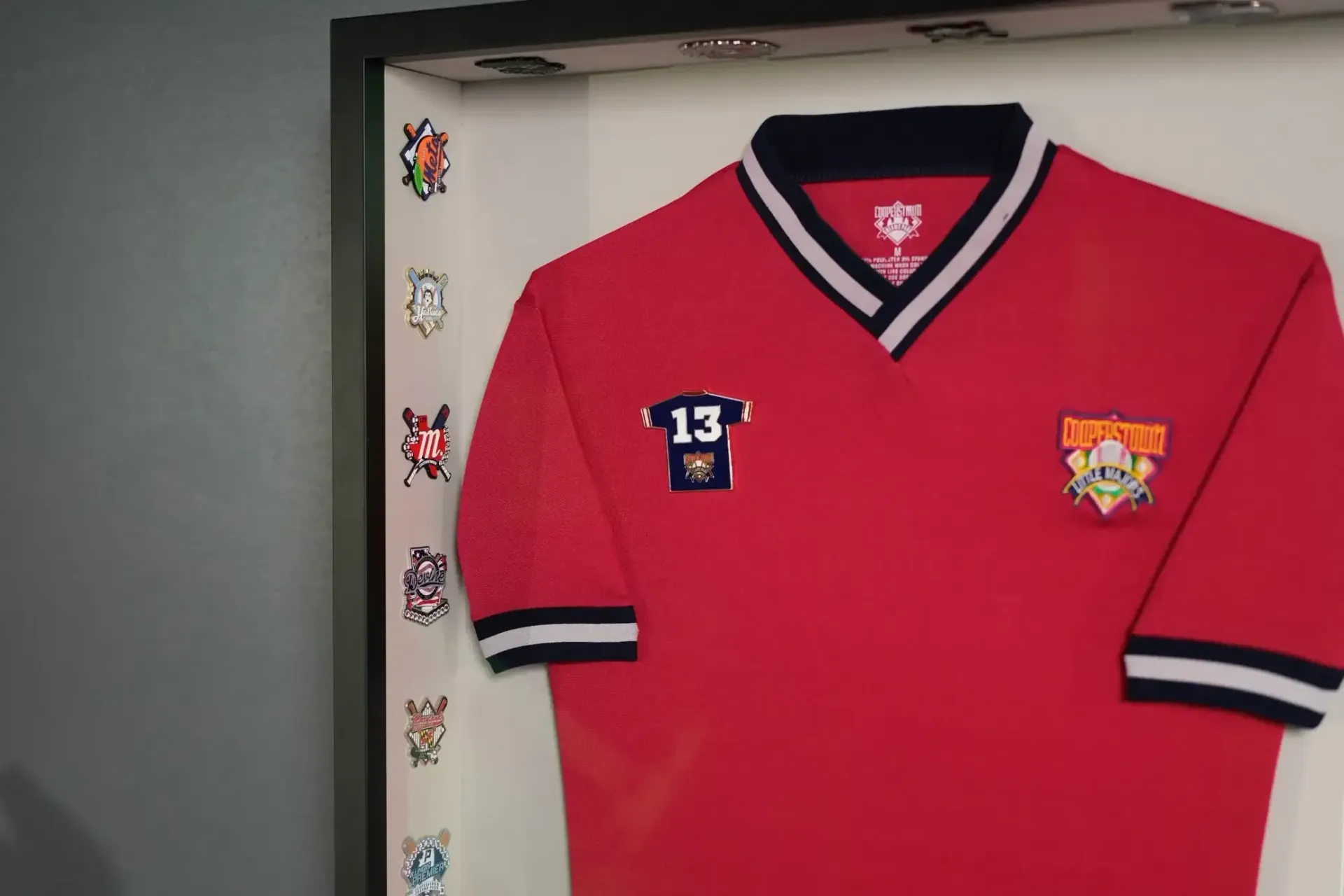 Red sports jersey with navy trim and club logos, displayed in a frame.