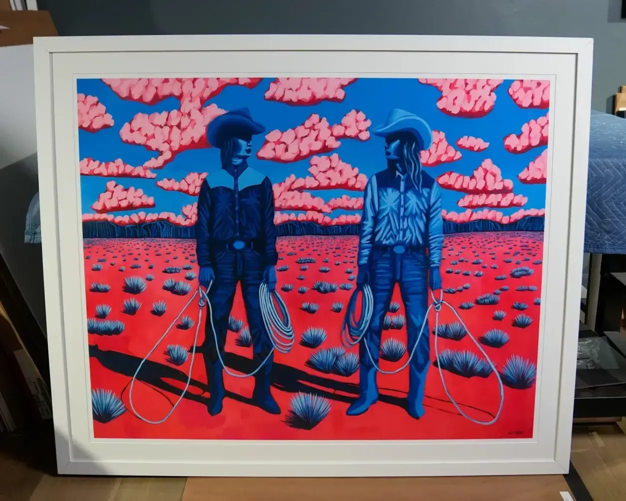 Two figures in hats stand in a red field under pink clouds and blue sky, holding ropes in a framed artwork.