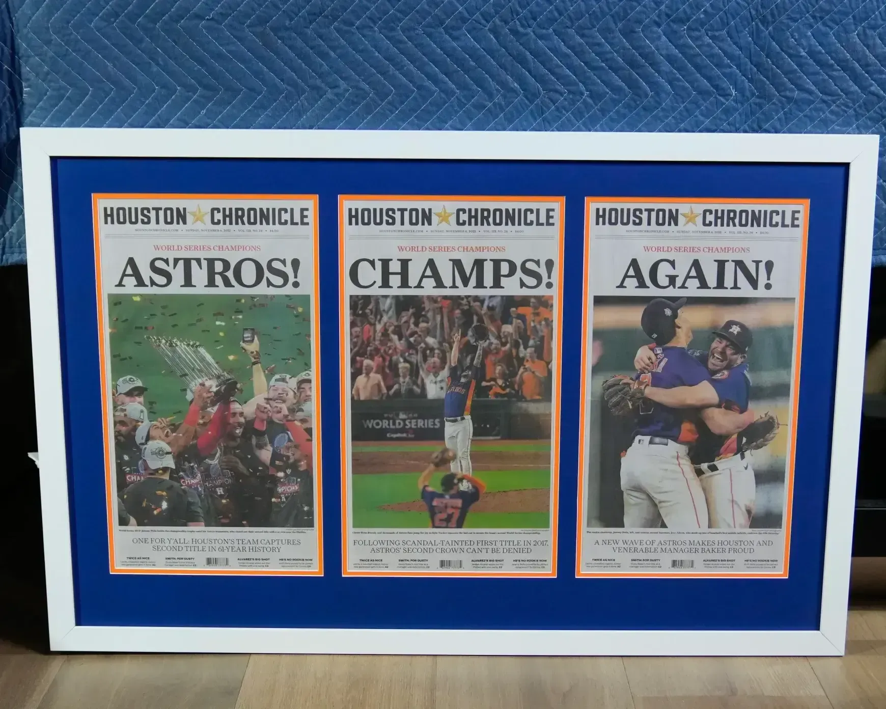 Three Houston Chronicle front pages on a blue board read “ASTROS!”, “CHAMPS!”, and “AGAIN!”