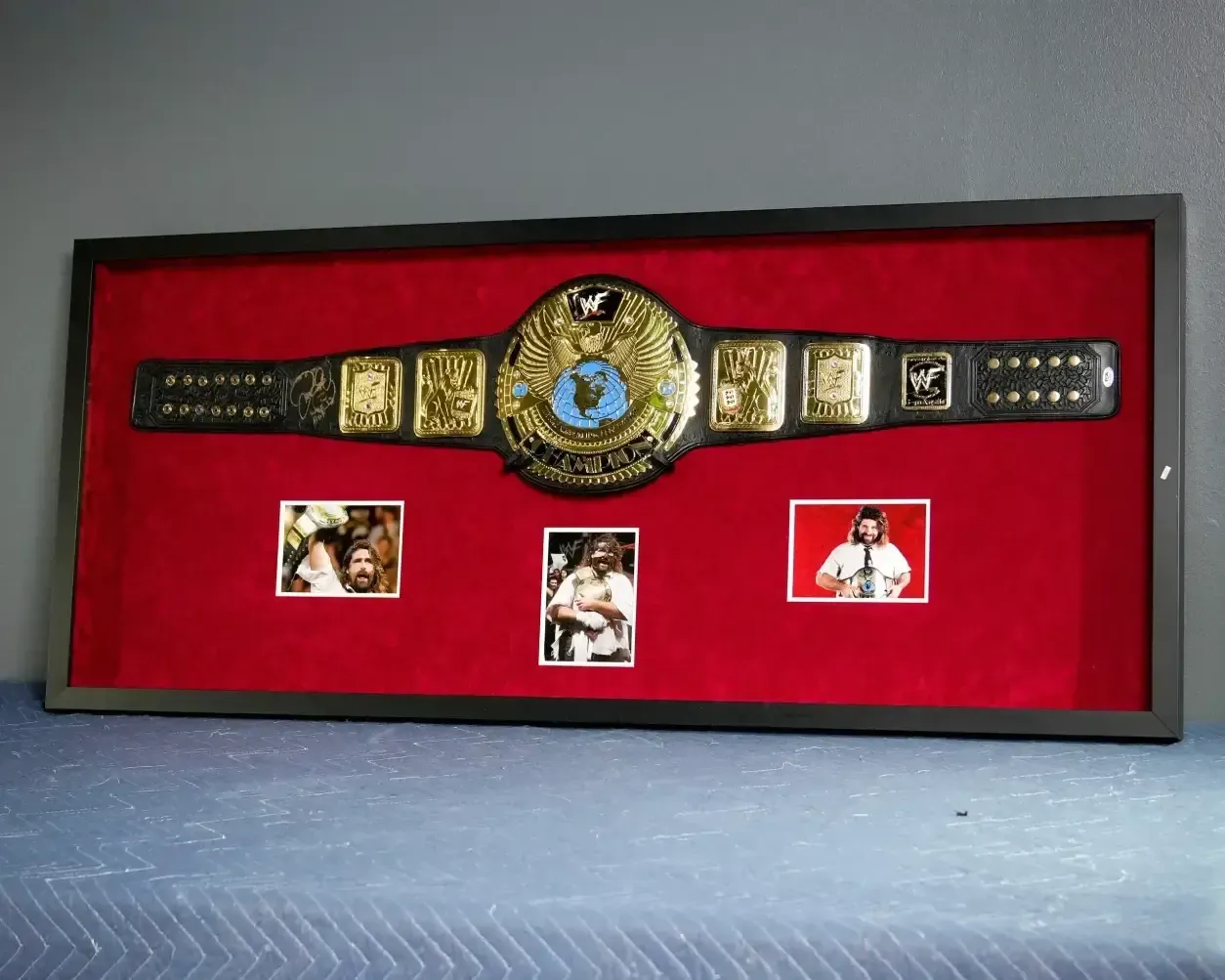 Framed championship belt displayed in a red case with three small photos below