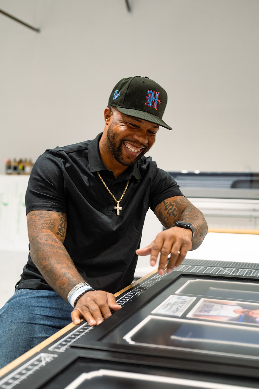 Man in black shirt and cap smiling while signing a framed item on a table