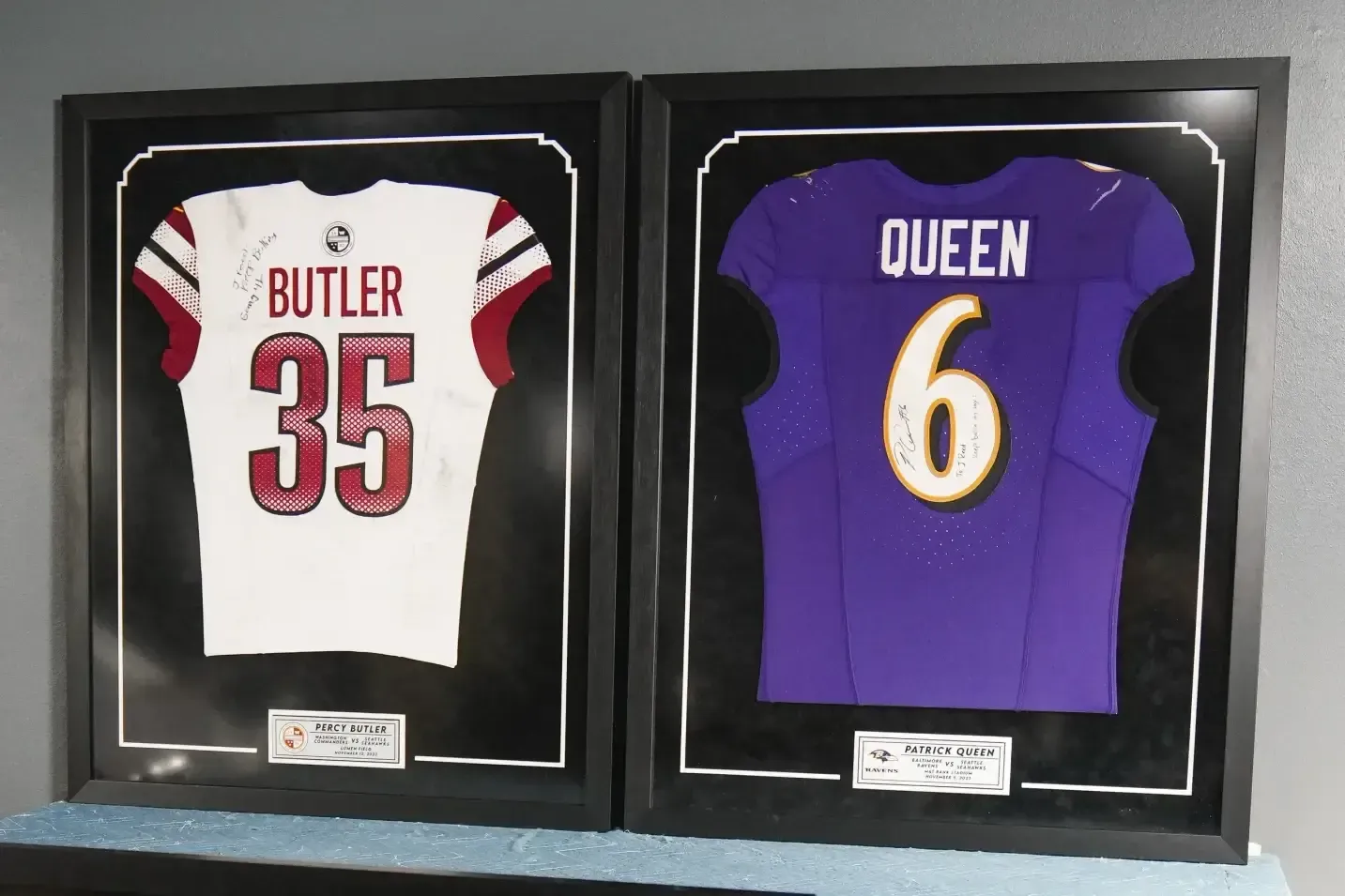 Framed football jerseys: white Butler #35 and purple Queen #6 side by side on a shelf