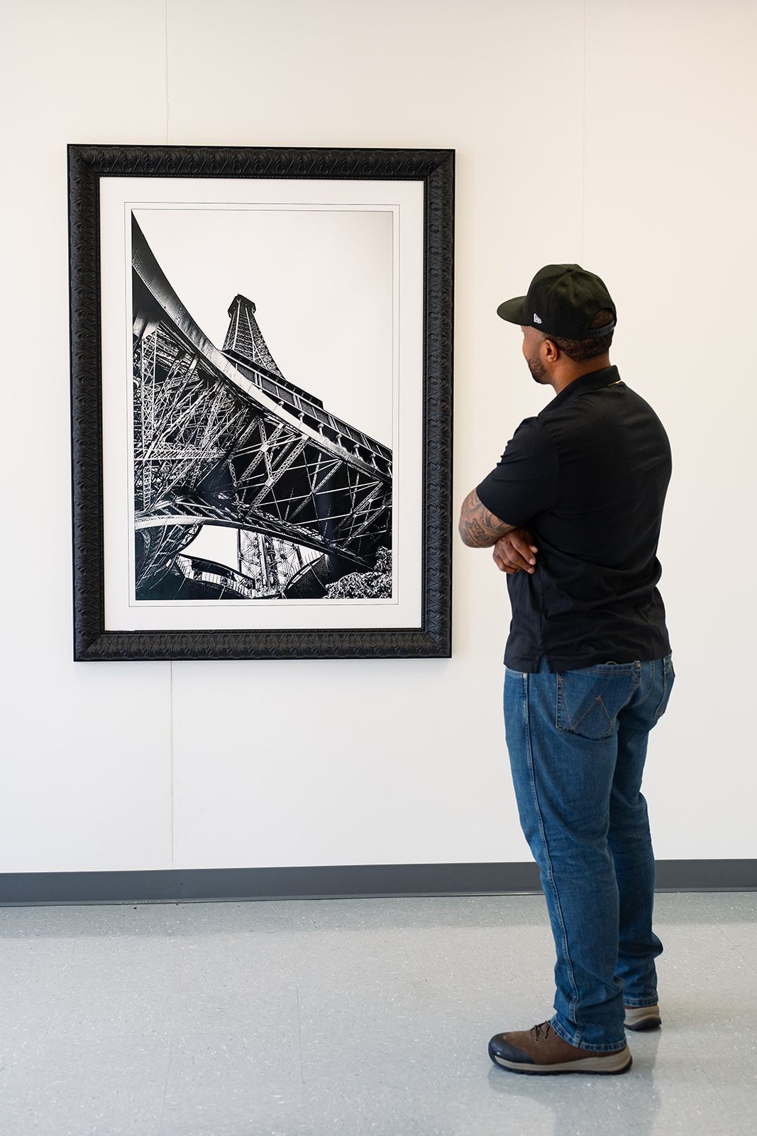 Person standing in a gallery, looking at a large black-and-white framed artwork on a white wall.