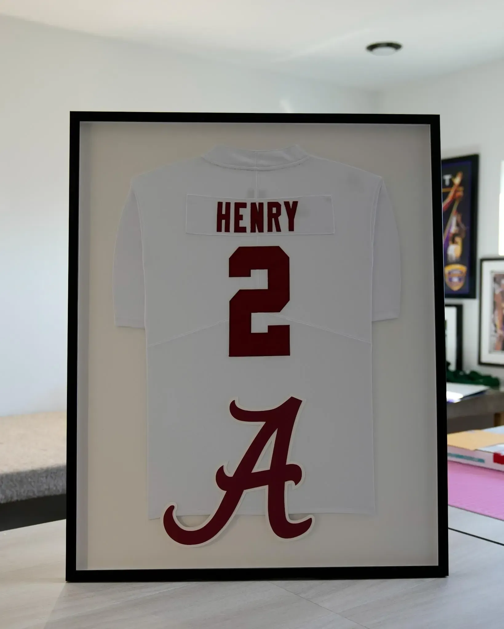 Framed white jersey with red “HENRY 2” and Alabama “A” on a wall