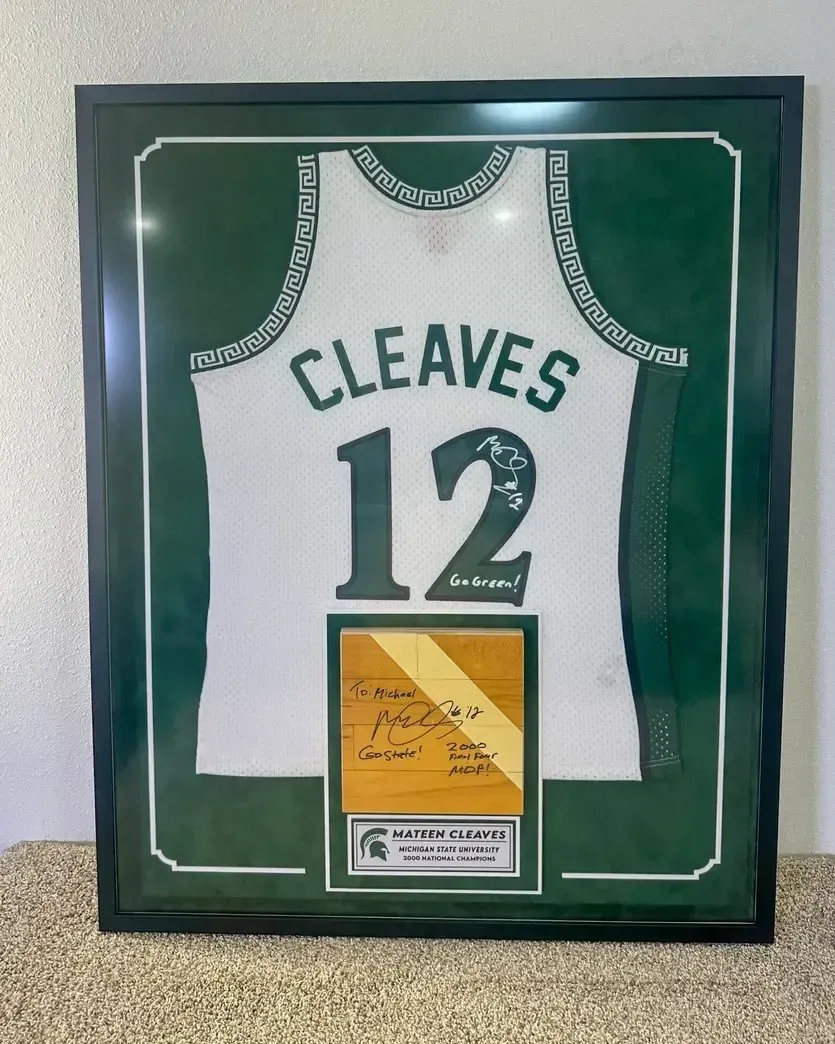 Framed green-and-white Cleveland baseball jersey with number 12 displayed on a wall.