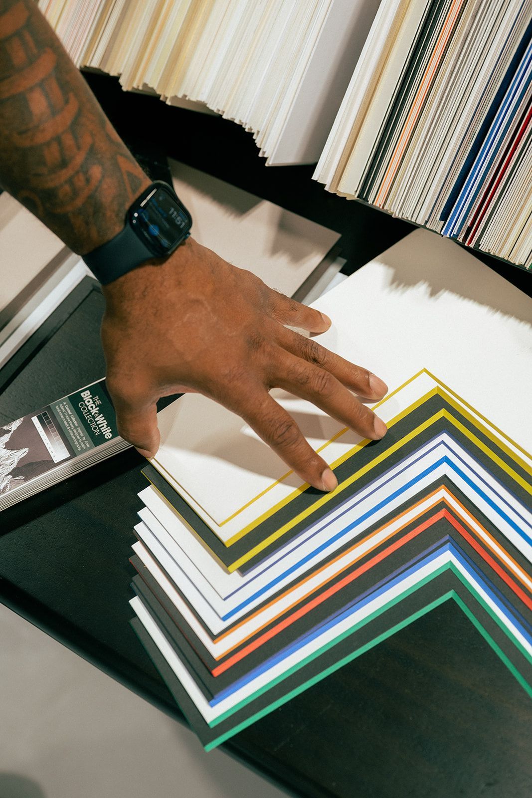 Hand flipping through a stack of colorful paper swatches on a desk