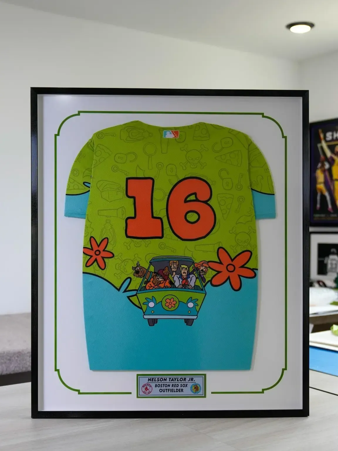 Framed display of a colorful green and blue sports jersey with the number 16 on a wall.
