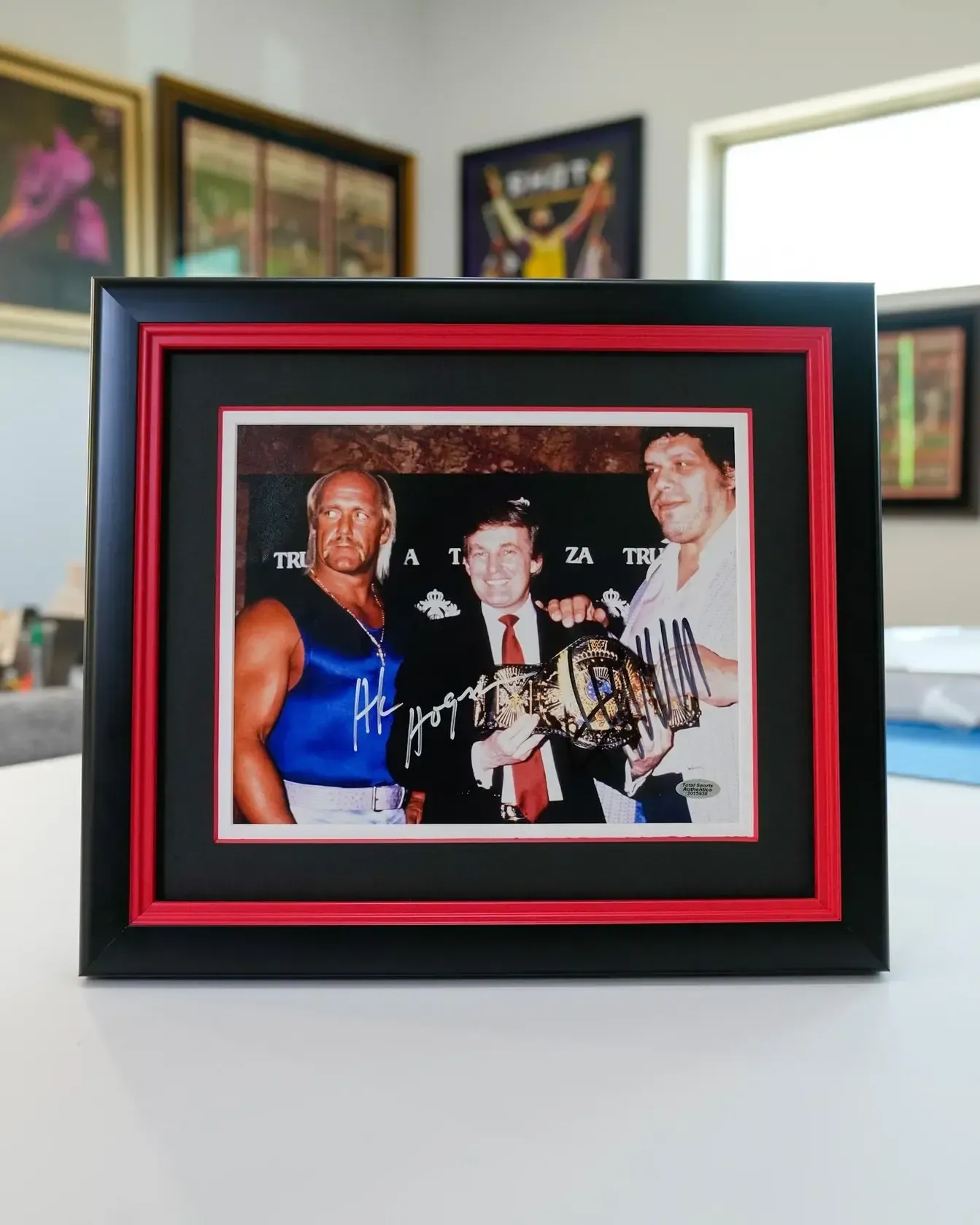 Framed photo of three people holding a championship belt, in a black and red frame on a table