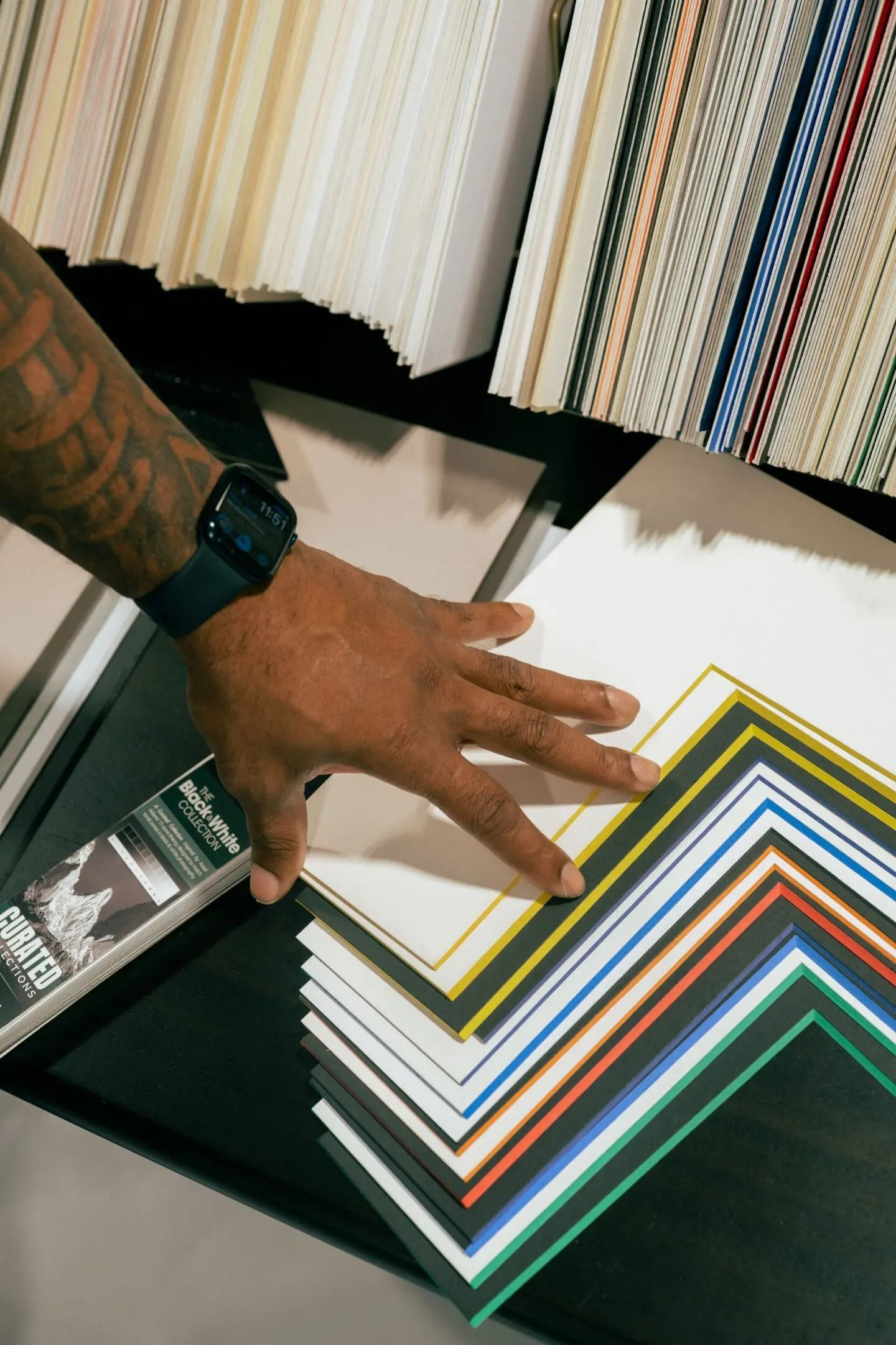 Hand reaching toward a fan of colorful cardstock samples on a table with fabric swatches in the background