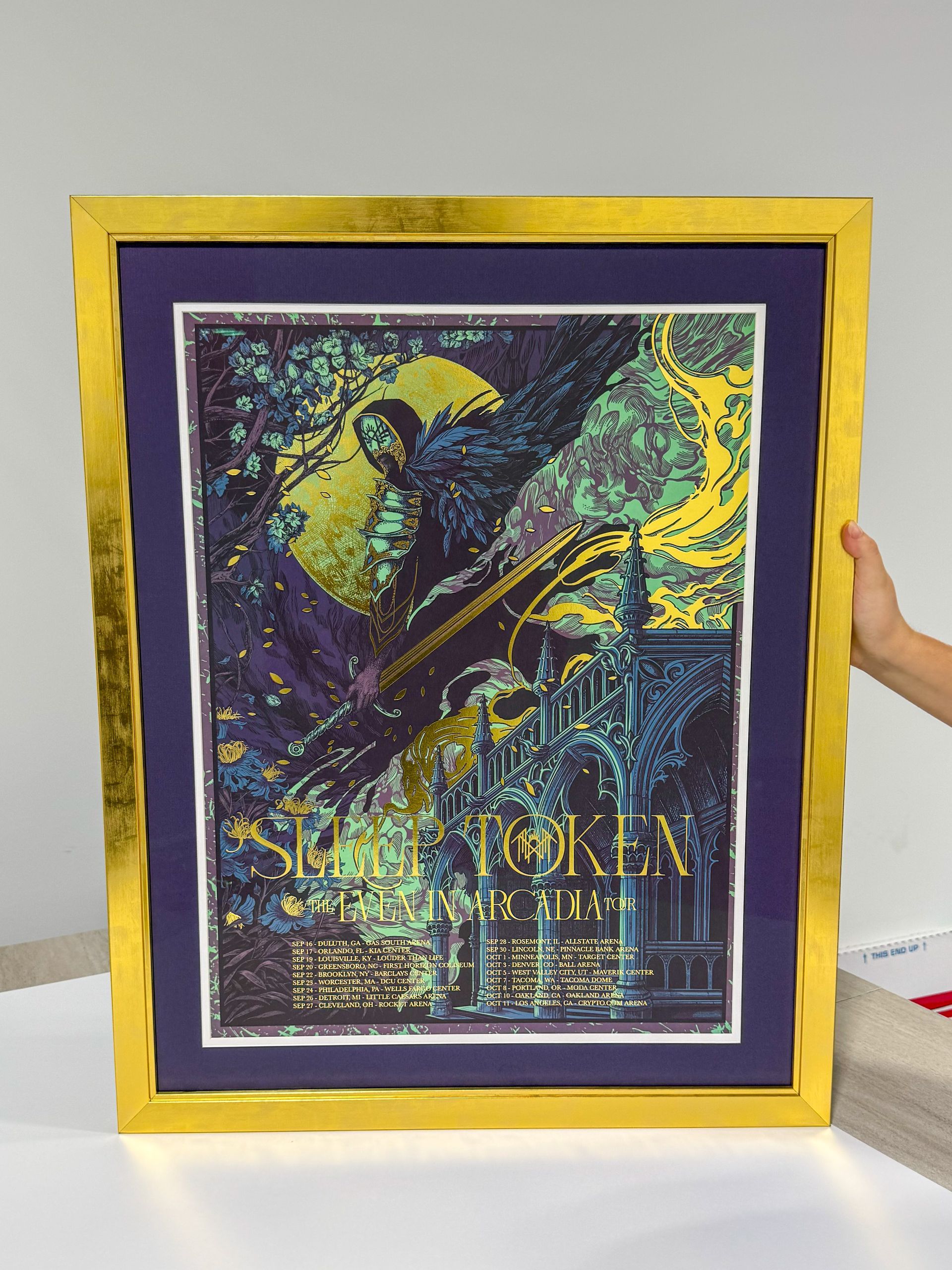 Framed abstract purple and gold art print with a yellow border, held upright against a white background