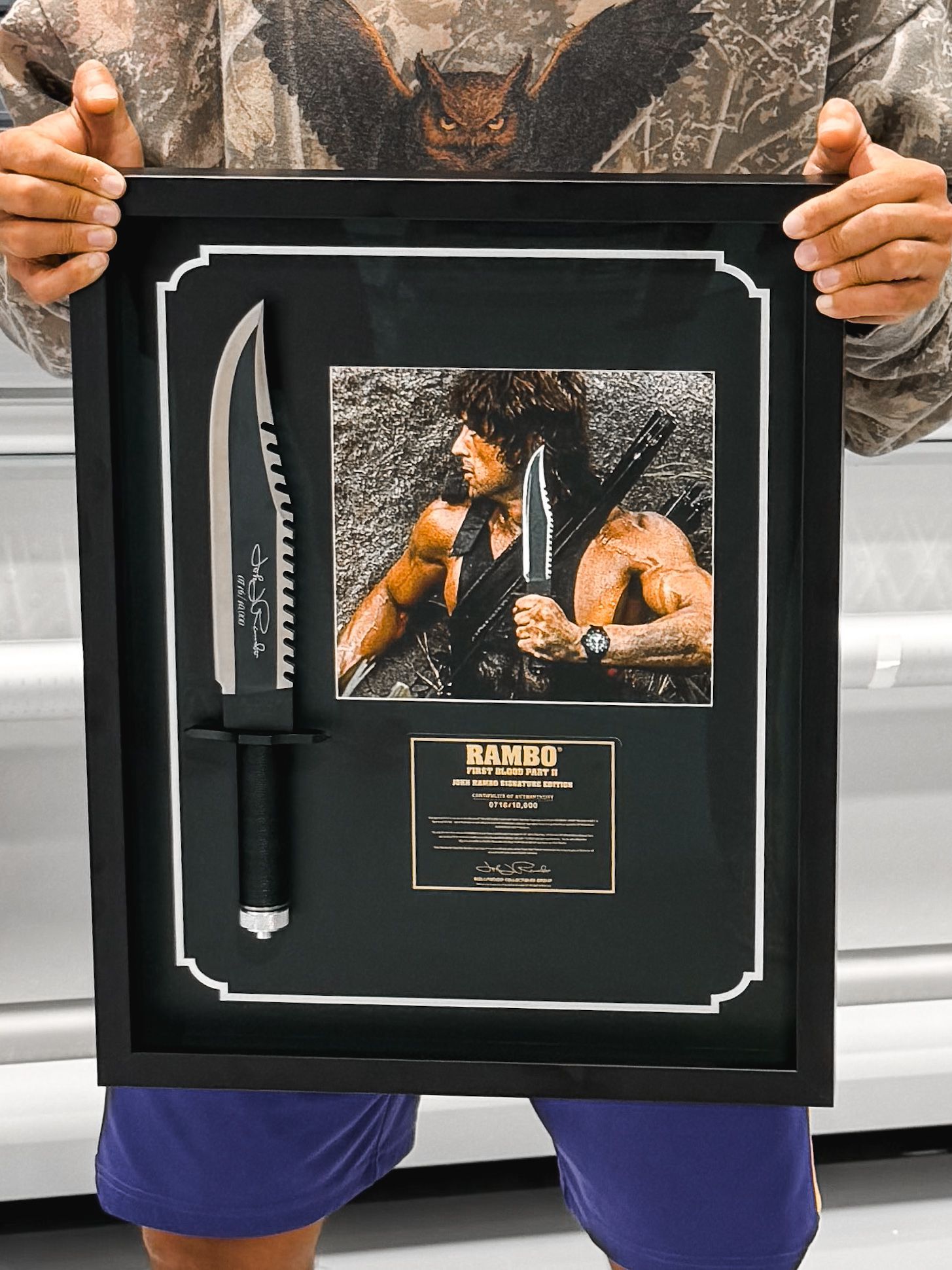 Person holding a framed UFC-style tribute collage with a knife and portrait in a black frame
