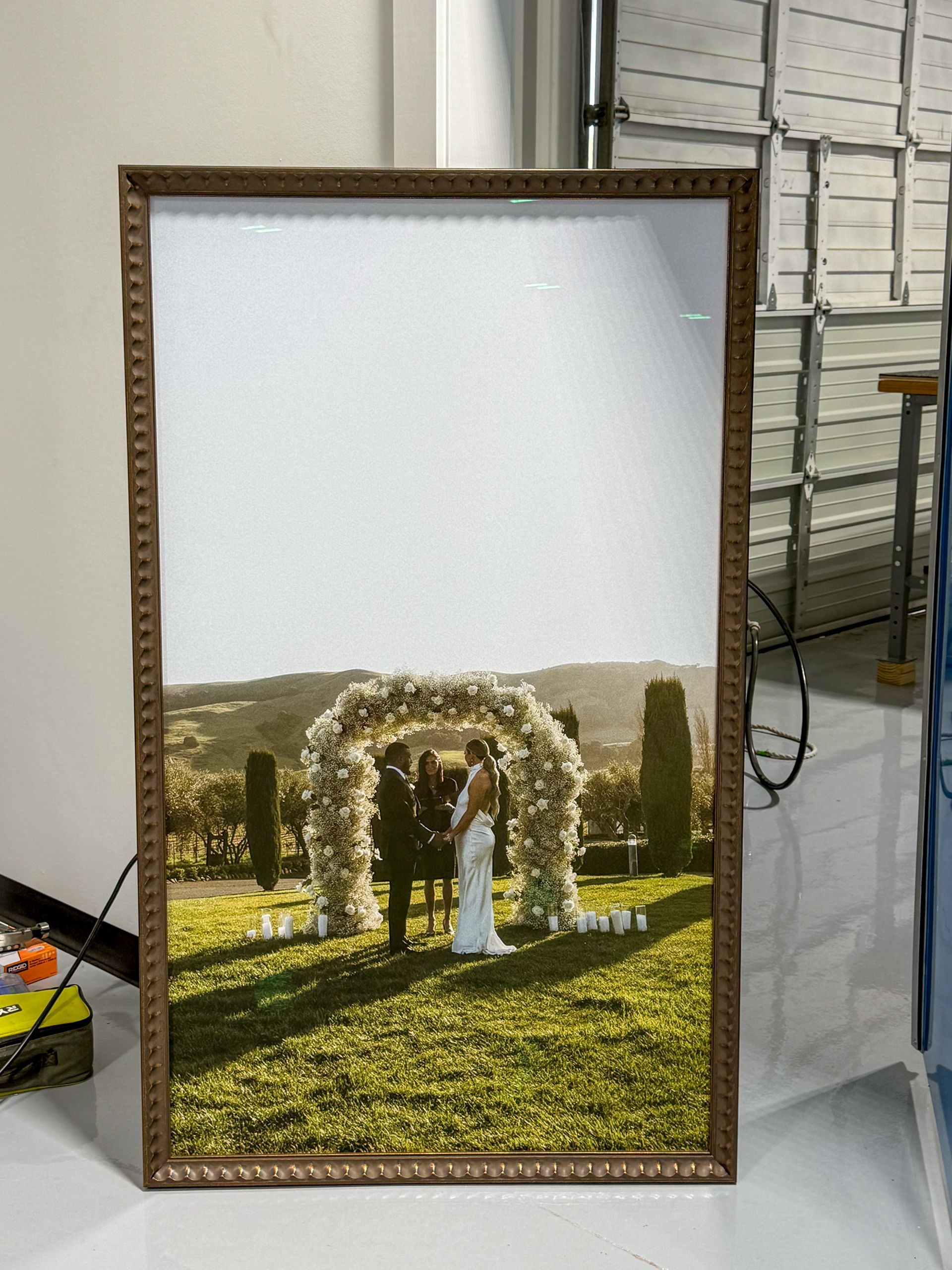 Framed photo of a white floral arch on a sunlit lawn with hills in the background