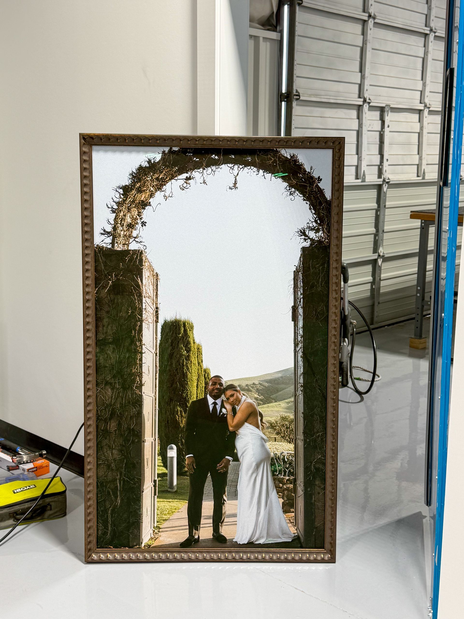 Framed wedding photo of a couple kissing beneath a leafy arch in an outdoor garden setting