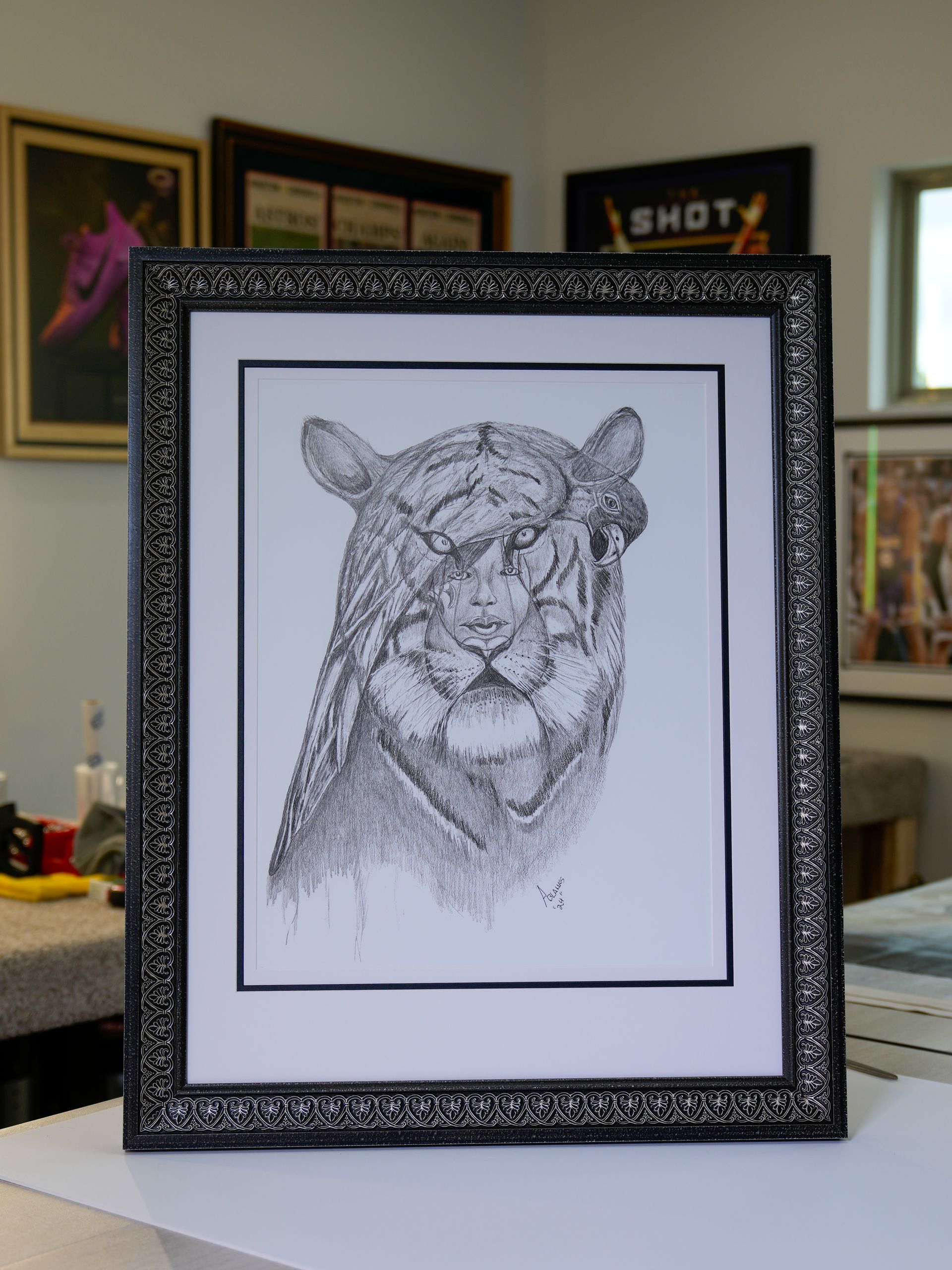 Framed black-and-white sketch of a leopard on a table in a room with wall art.
