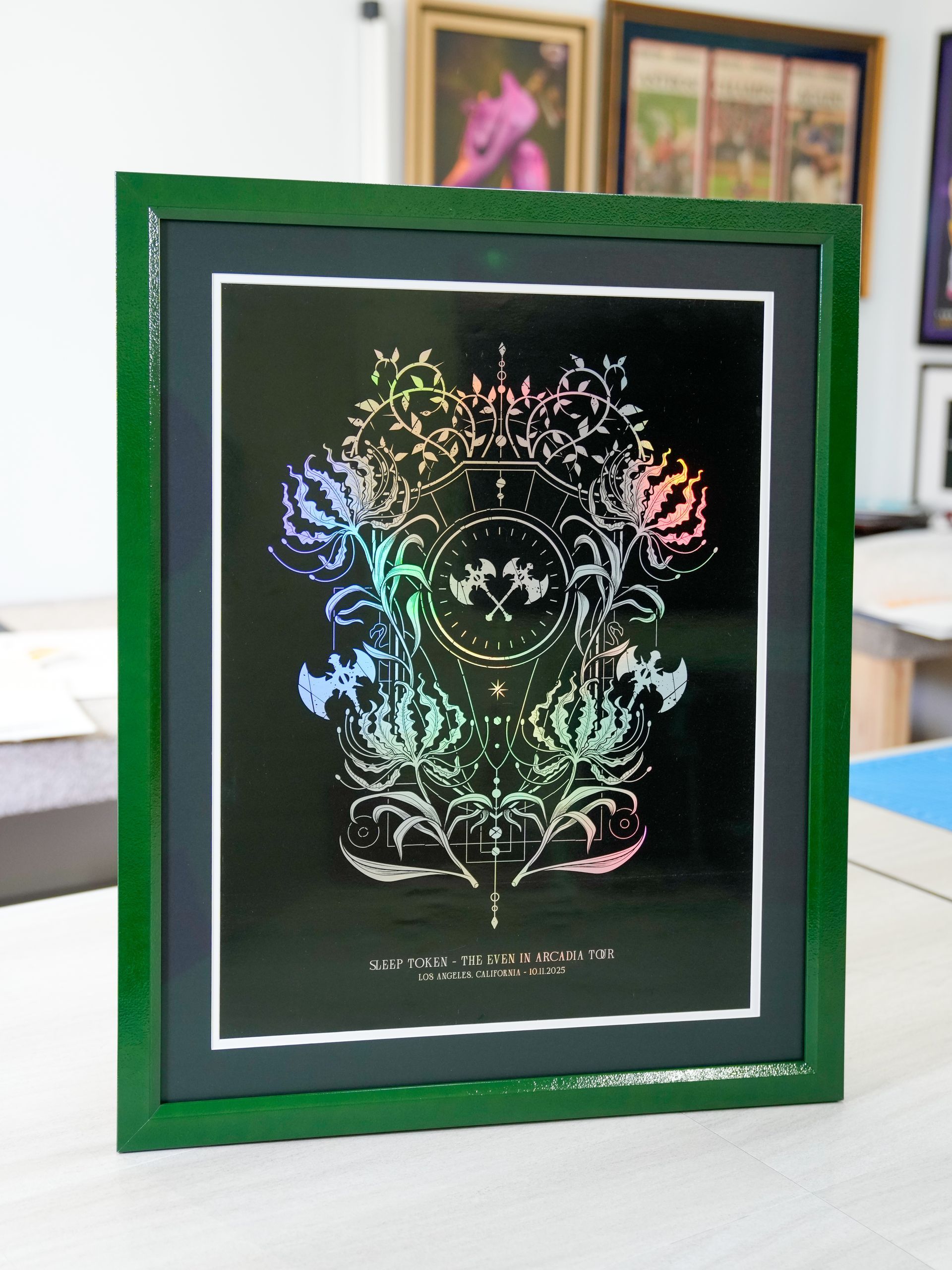 Framed black artwork with colorful floral and butterfly-like design on a green frame, on a table indoors