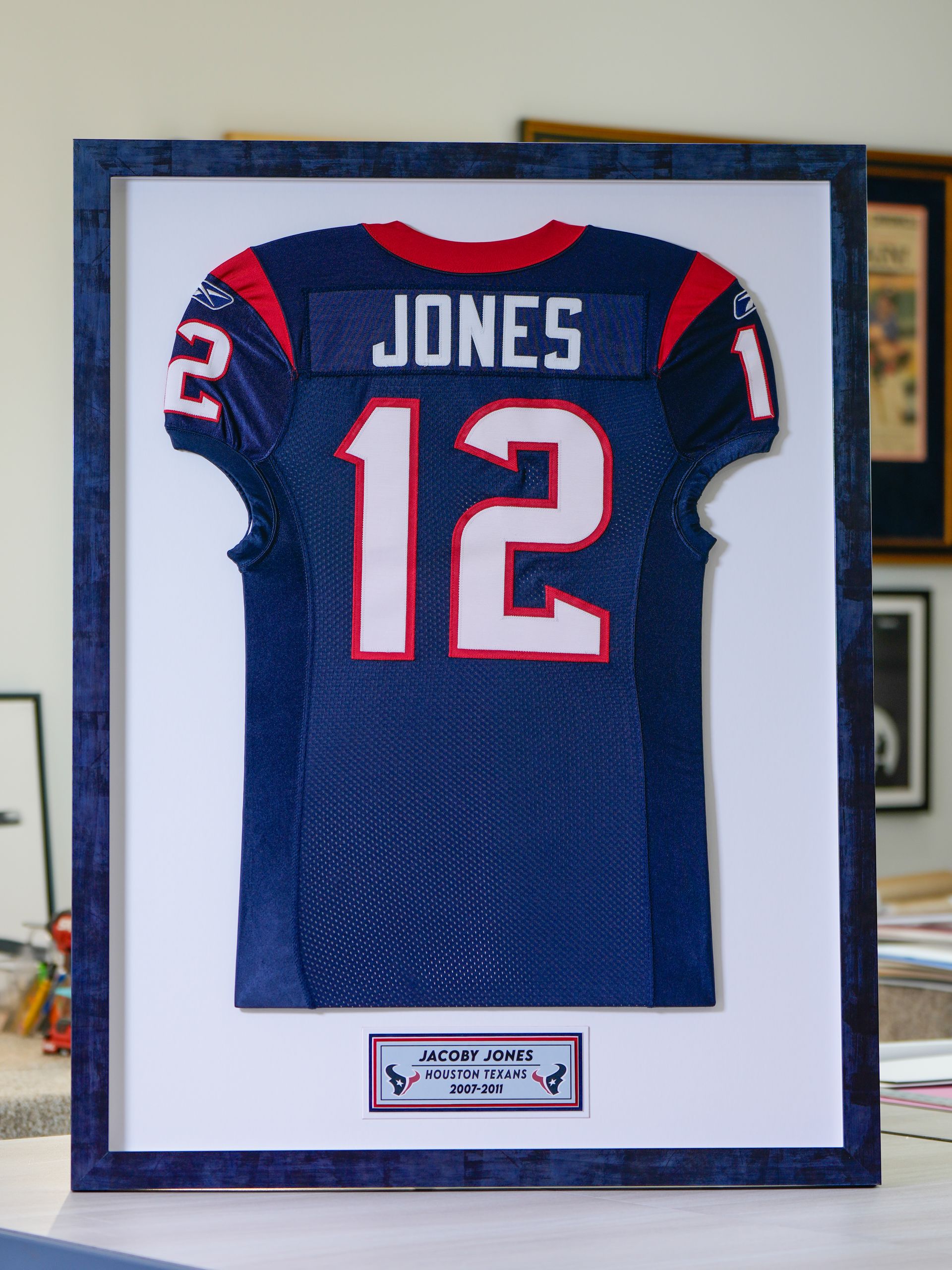 Framed navy football jersey with red-and-white trim, name JONES and number 12, displayed on a wall
