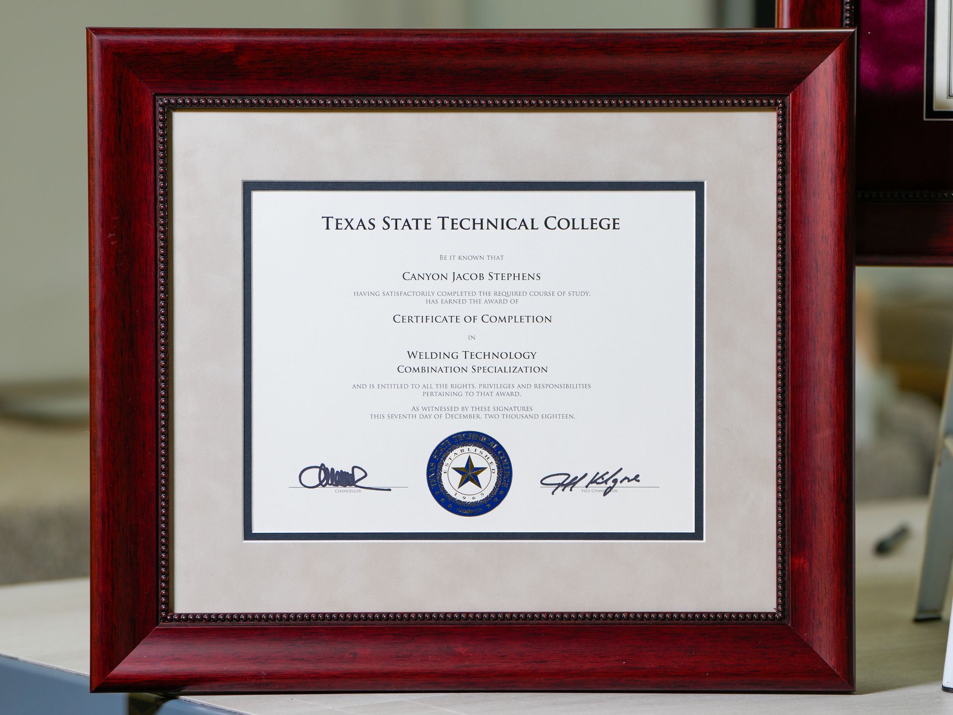 Framed Texas State Technical College diploma with red wood frame and seal on a table