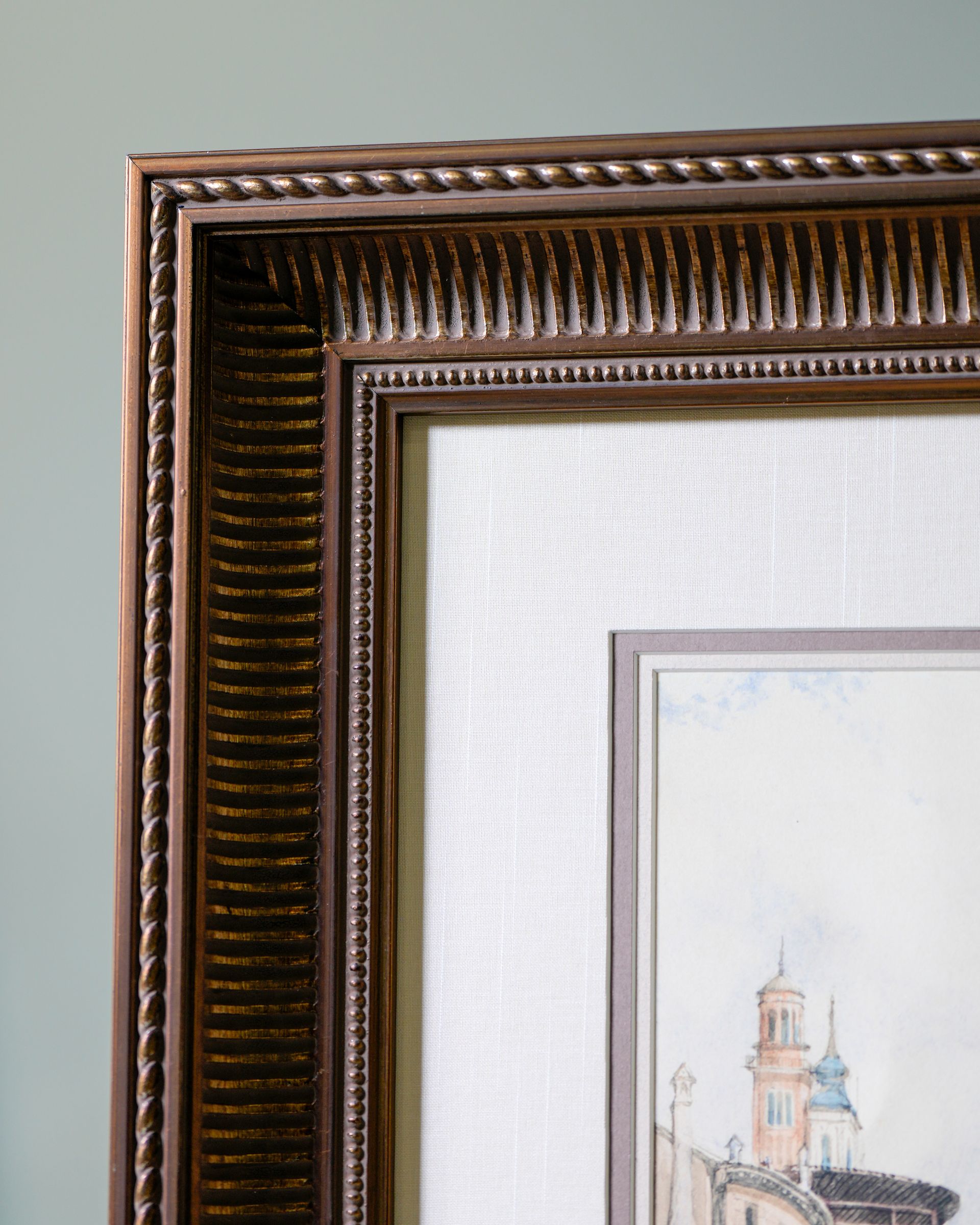 Close-up of an ornate brown picture frame with a smaller framed artwork inside on a light wall
