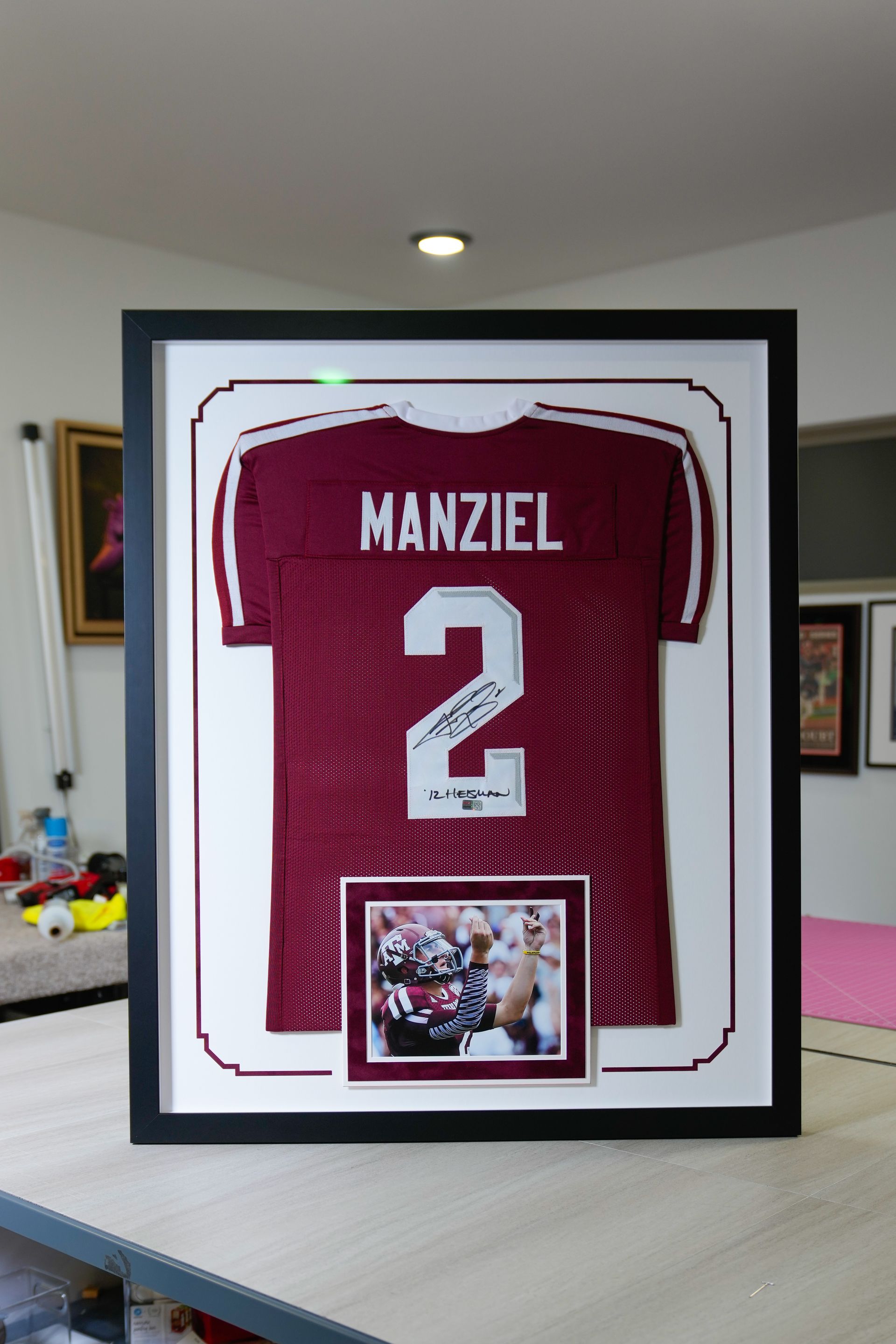 Framed maroon Manziel #2 football jersey with a small action photo at the bottom on a table.