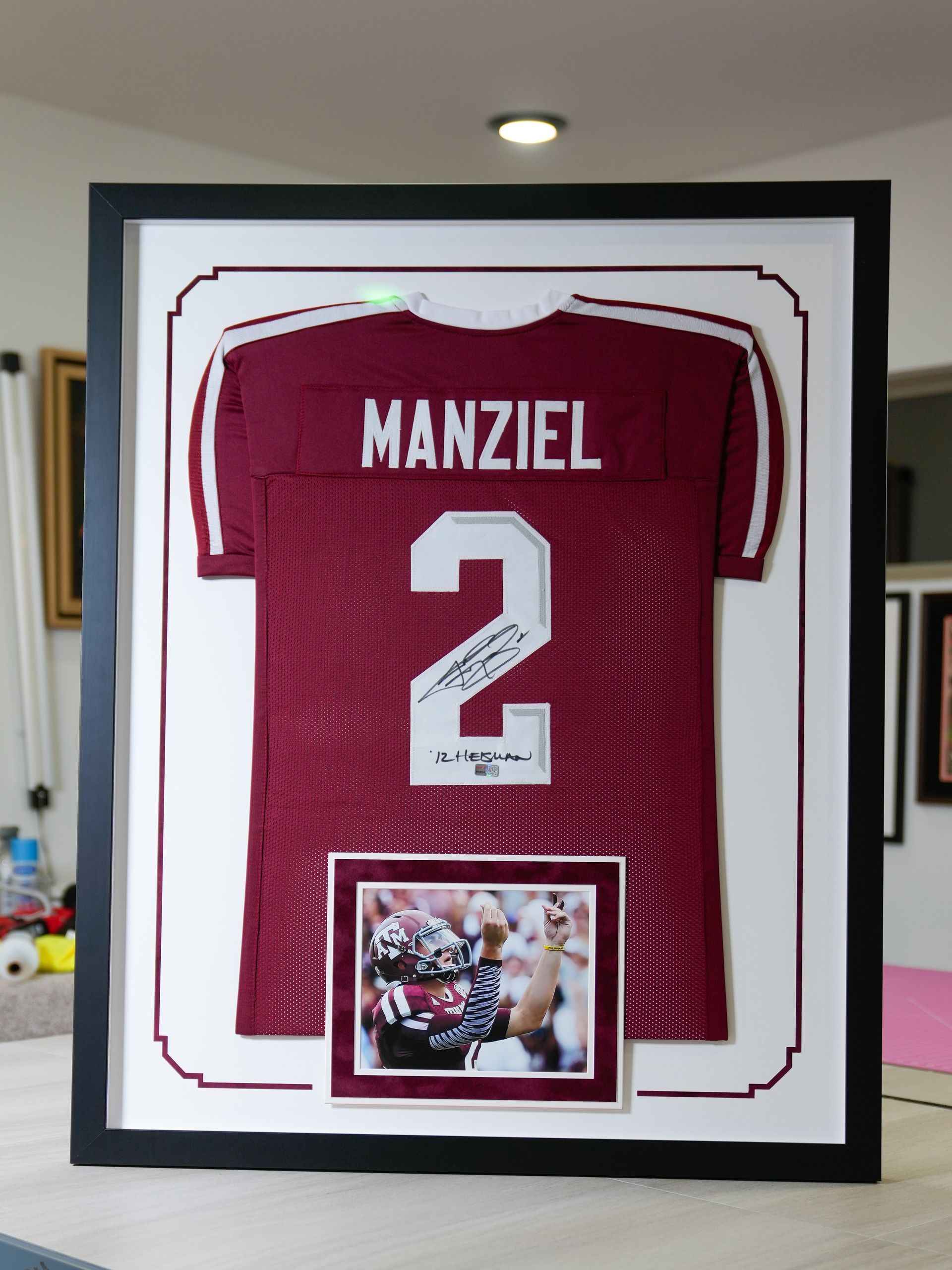 Framed maroon Manziel #2 football jersey with a small photo beneath it on a wall