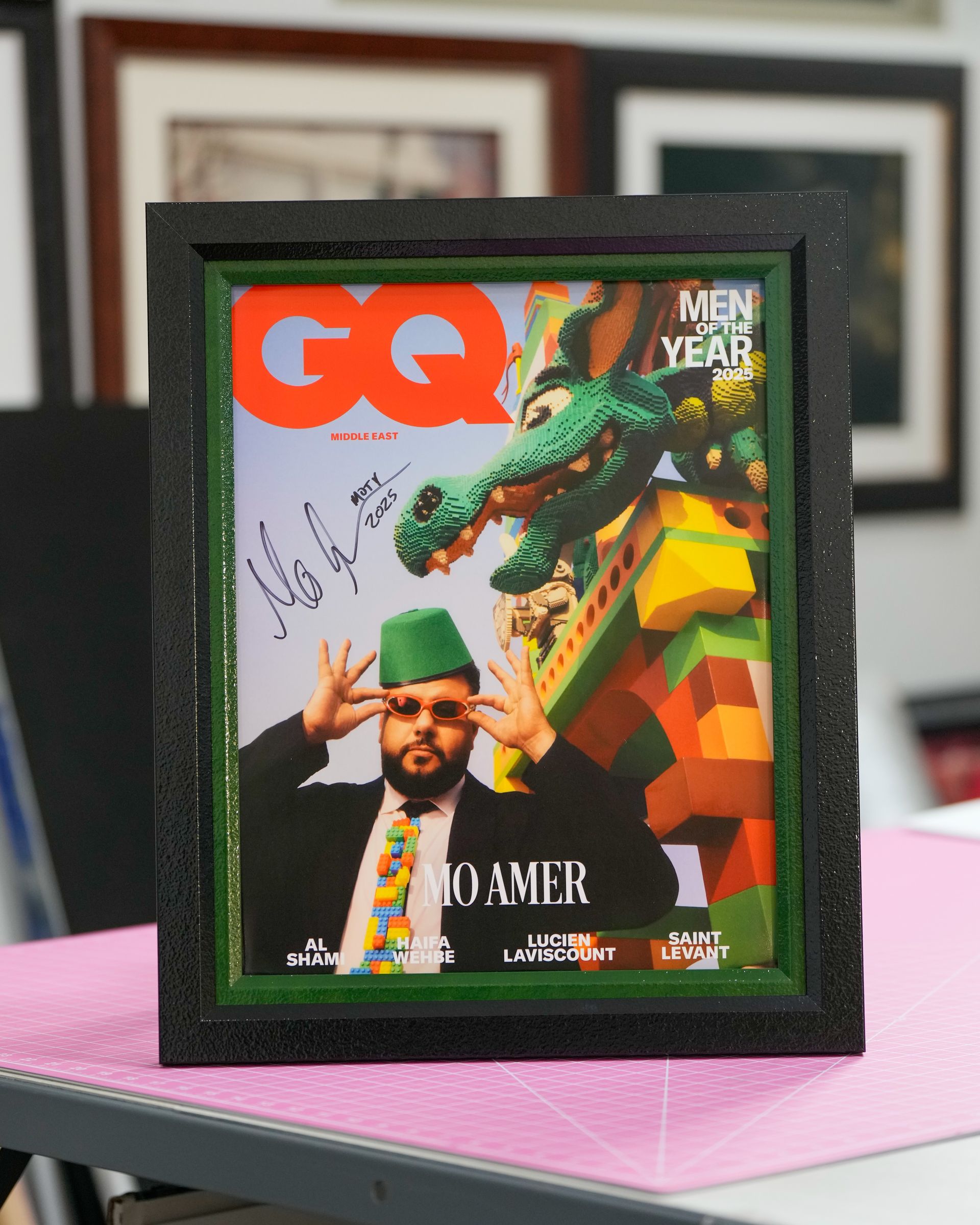 Framed GQ magazine cover with a colorful portrait and green crocodile artwork on a pink table