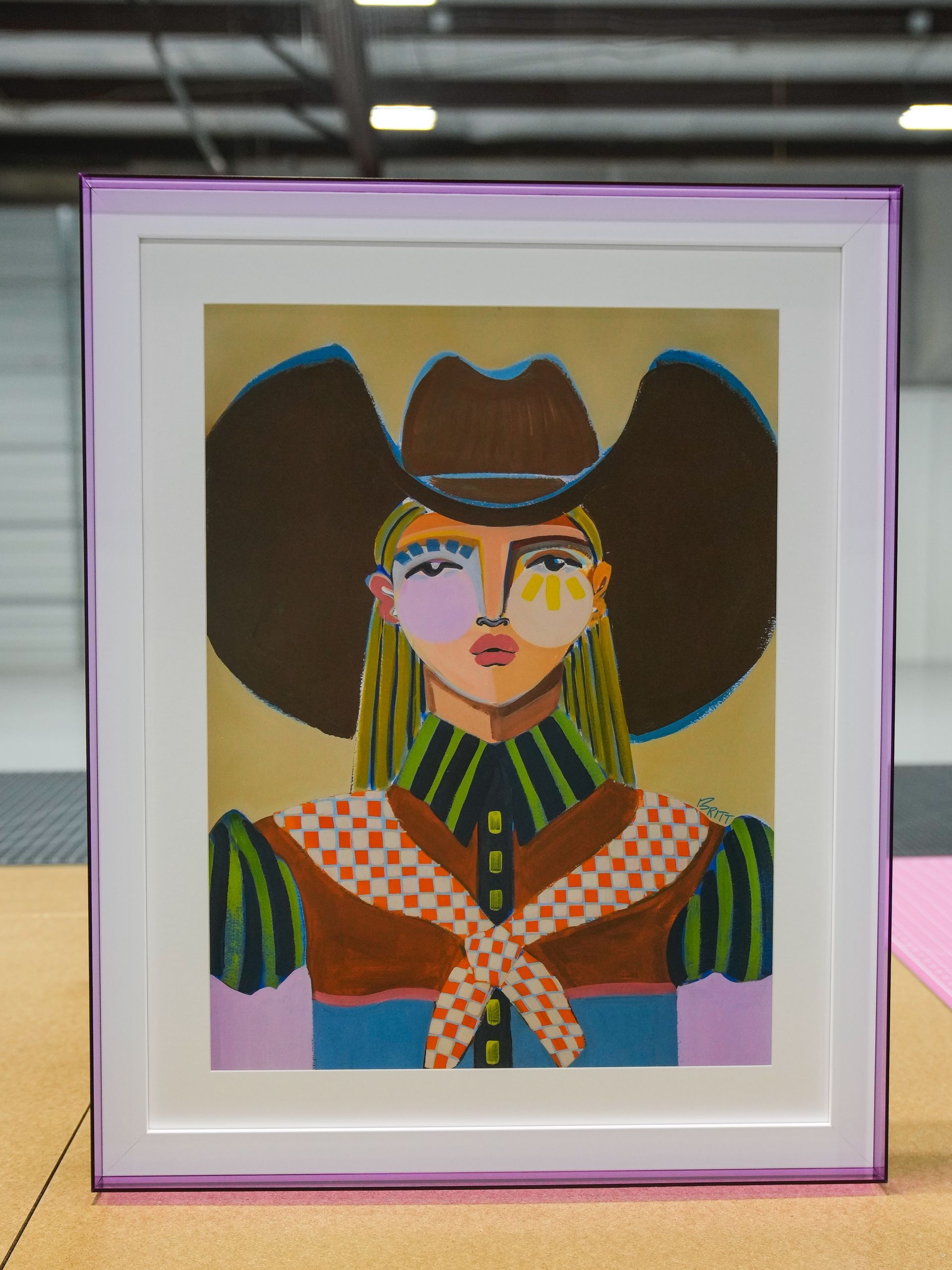 Framed colorful portrait of a person in a wide-brimmed hat and patterned clothing