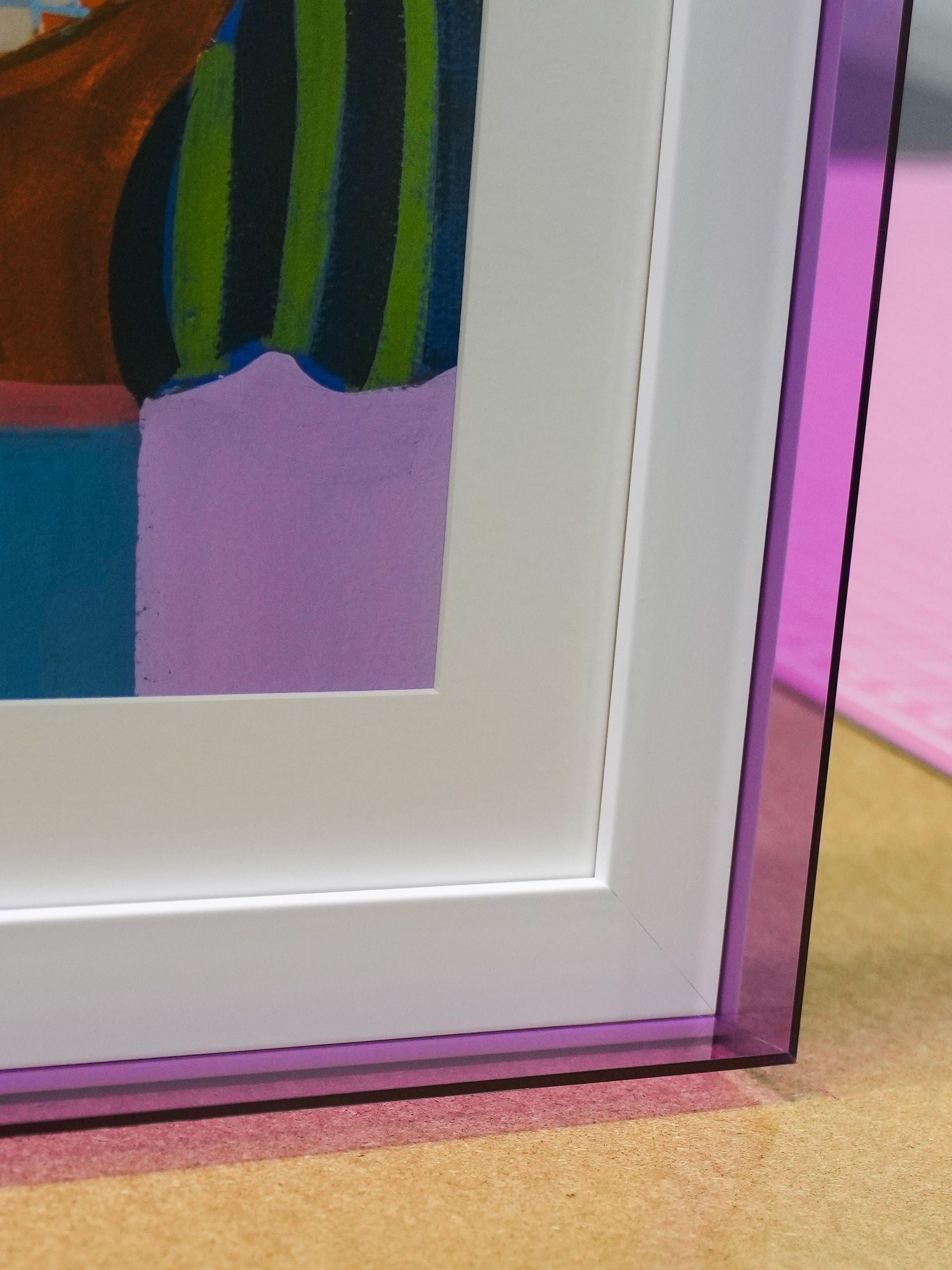 Close-up of a framed artwork with a white mat and purple border against a pink wall.