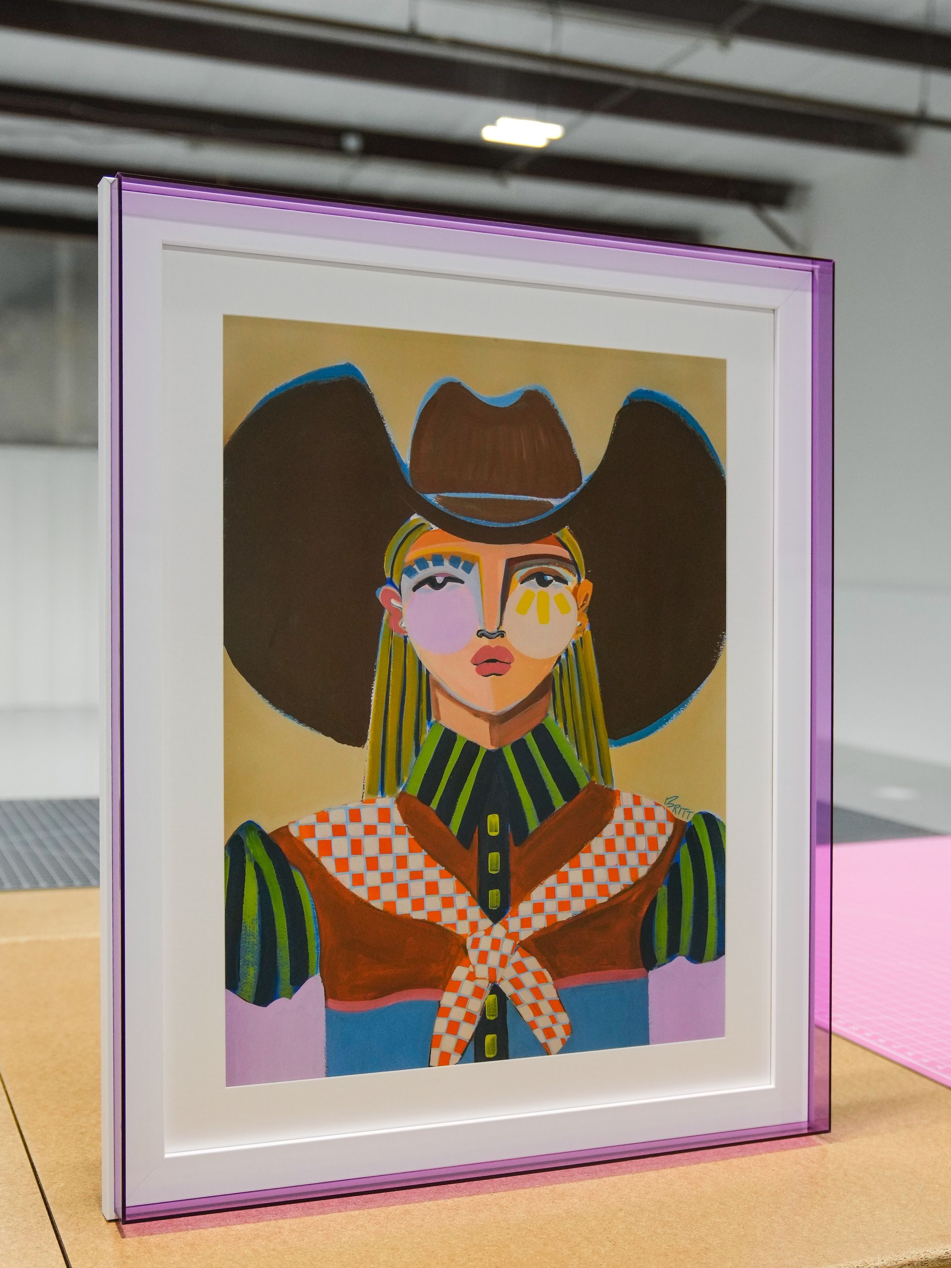 Framed colorful portrait of a person in a cowboy hat with a patterned scarf and striped sleeves
