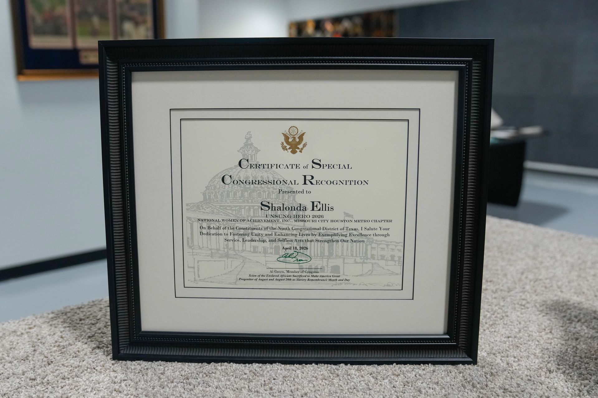 Framed certificate in a black frame on a speckled countertop, with blurred office background
