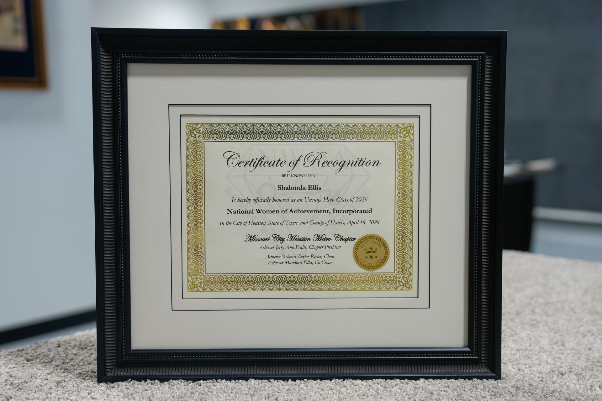 Framed gold-bordered certificate displayed on a tabletop