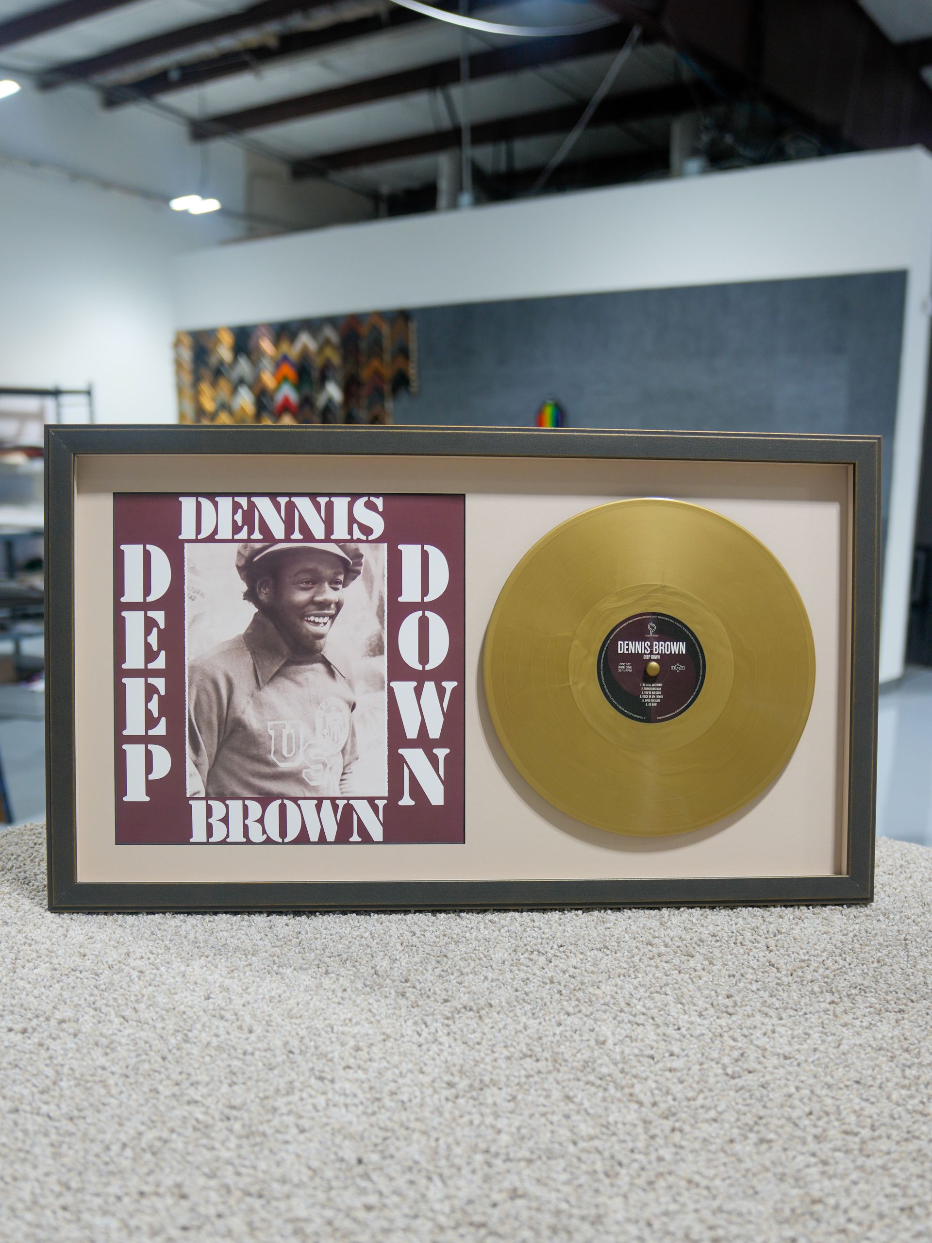 Framed Dennis Brown album artwork with a gold record displayed in a gallery setting