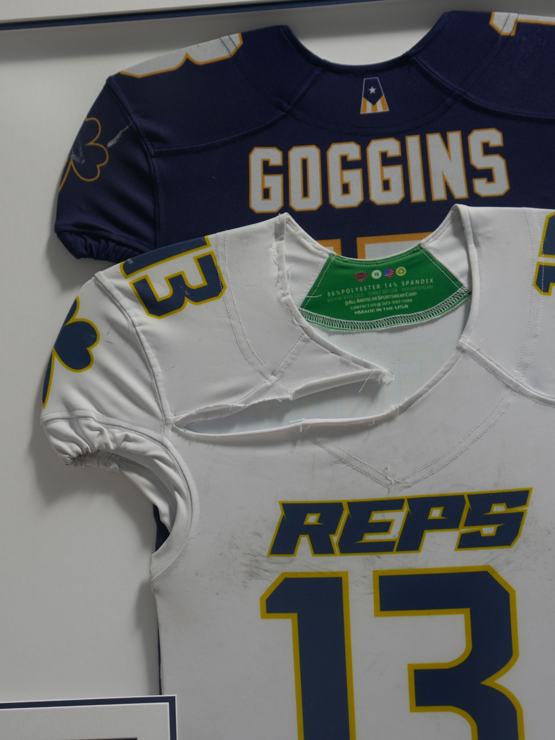 Two hanging football jerseys, navy “COGGINS” and white “REPS 13,” with yellow accents