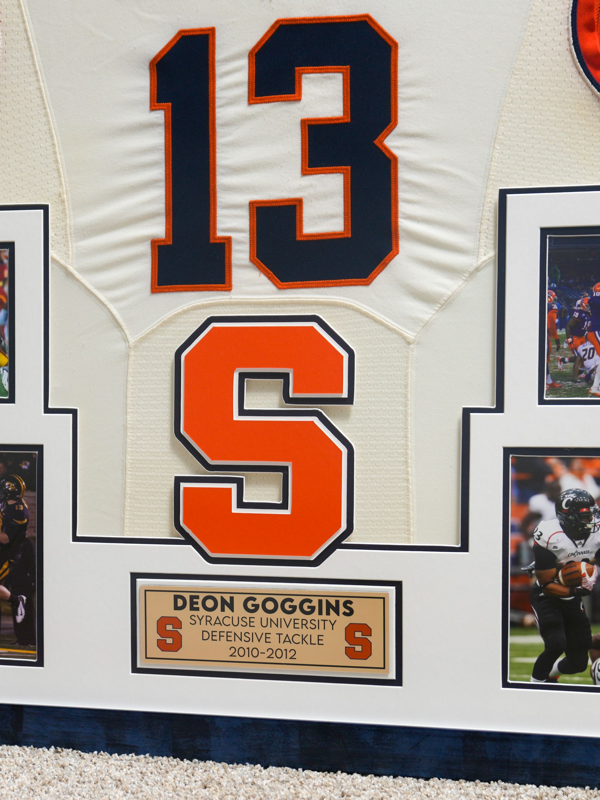 Framed white jersey with orange-outlined number 13, a large orange S, and a Lion Goggins plaque underneath