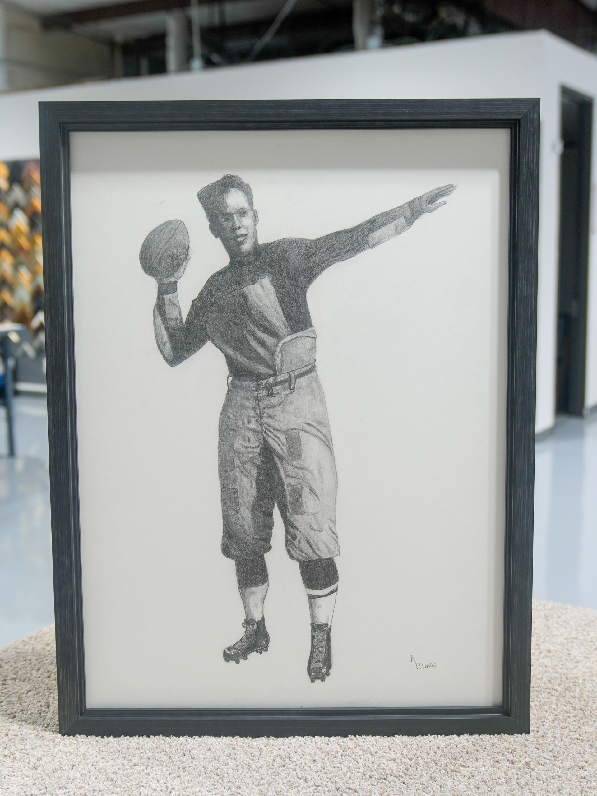 Framed black-and-white sketch of a football player holding a ball and throwing in a kiosk display