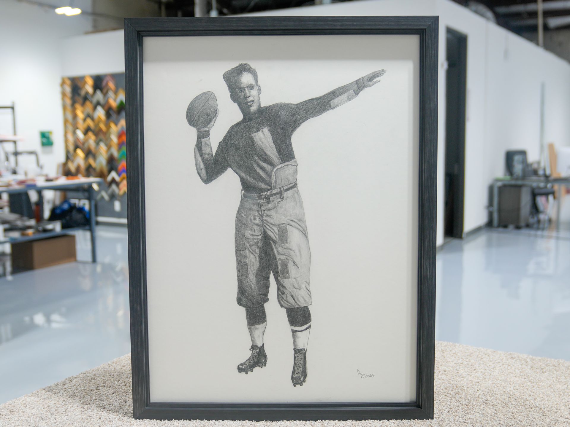Framed black-and-white drawing of a baseball player holding a ball and pointing, displayed in a gallery.