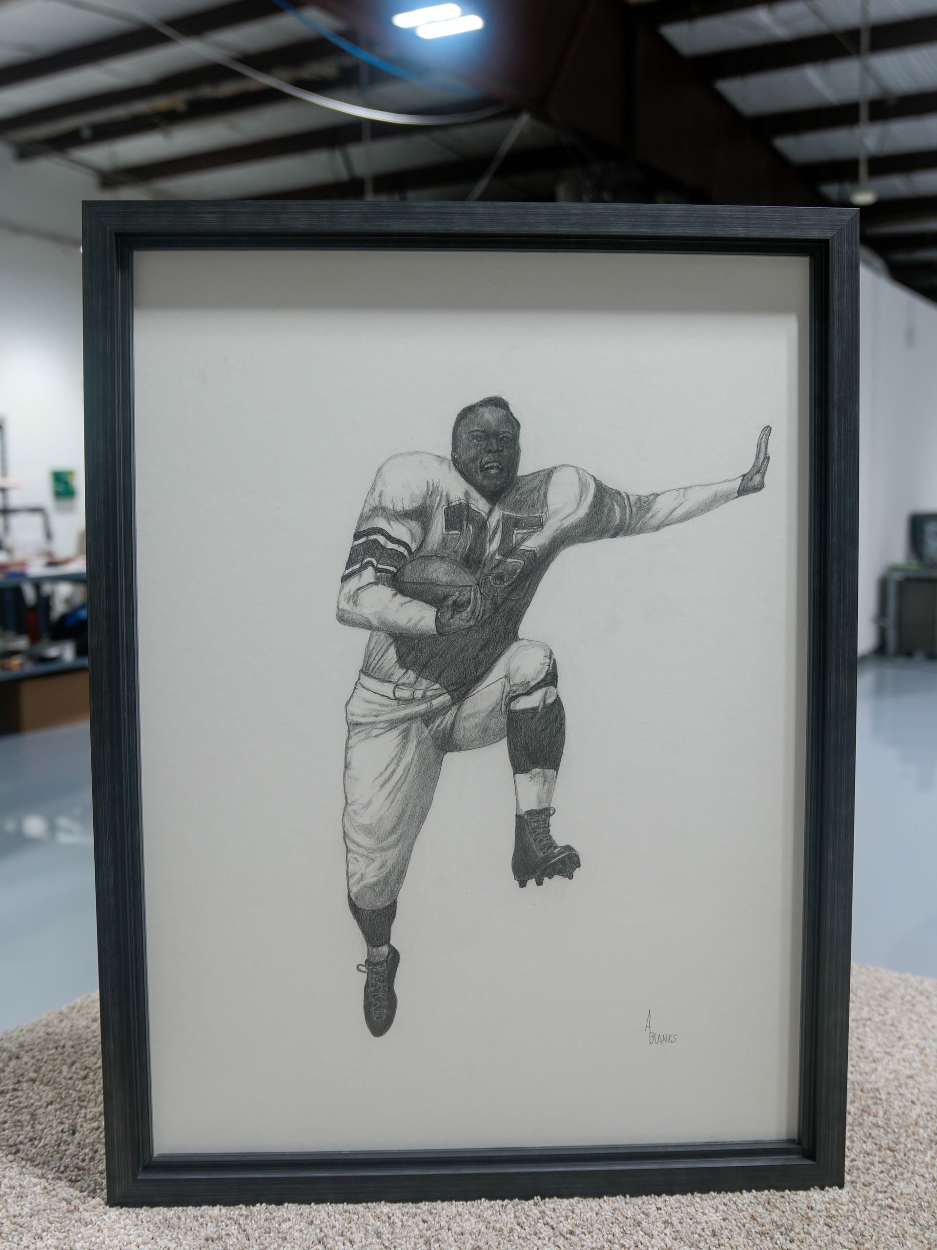 Framed black-and-white drawing of a football player running with the ball on a white background