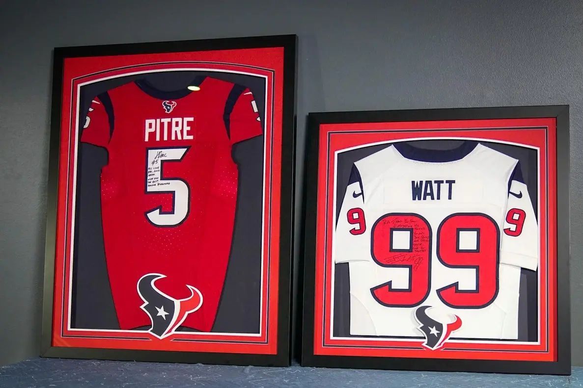 Framed Houston Texans jerseys: red Andre Johnson No. 5 and white J.J. Watt No. 99 on a wall