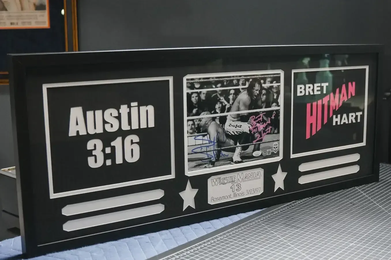 Black wrestling-themed sign with “Austin 3:16,” a match photo, and “Bret “Hitman” Hart” on a black background