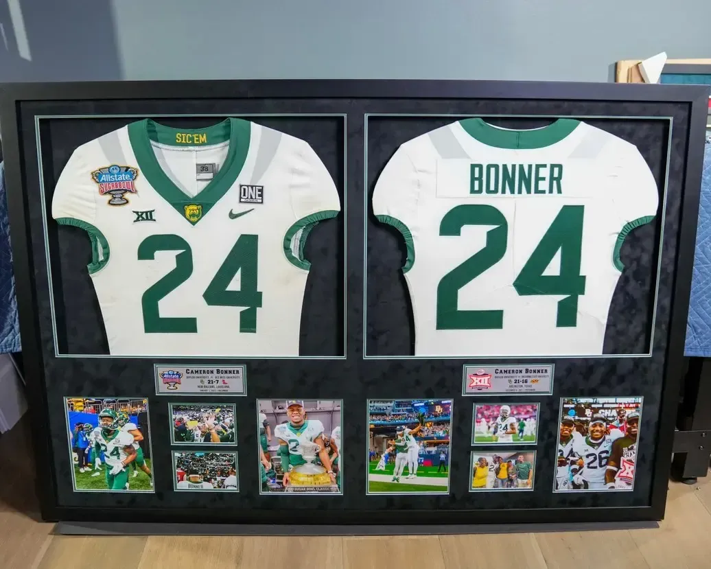 Framed football jersey display with white and green jerseys numbered 24 and sports cards beneath