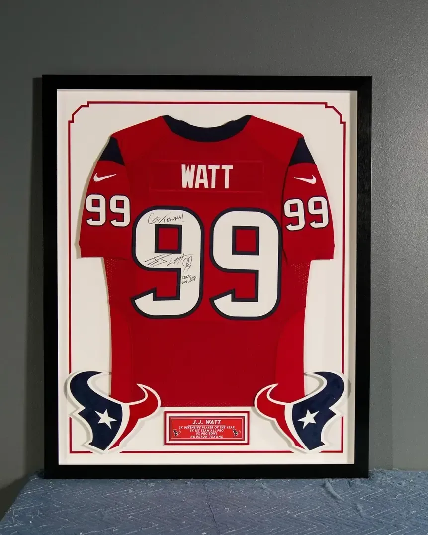 Framed red Houston Texans jersey with number 99 and name Watt, displayed on a wall.