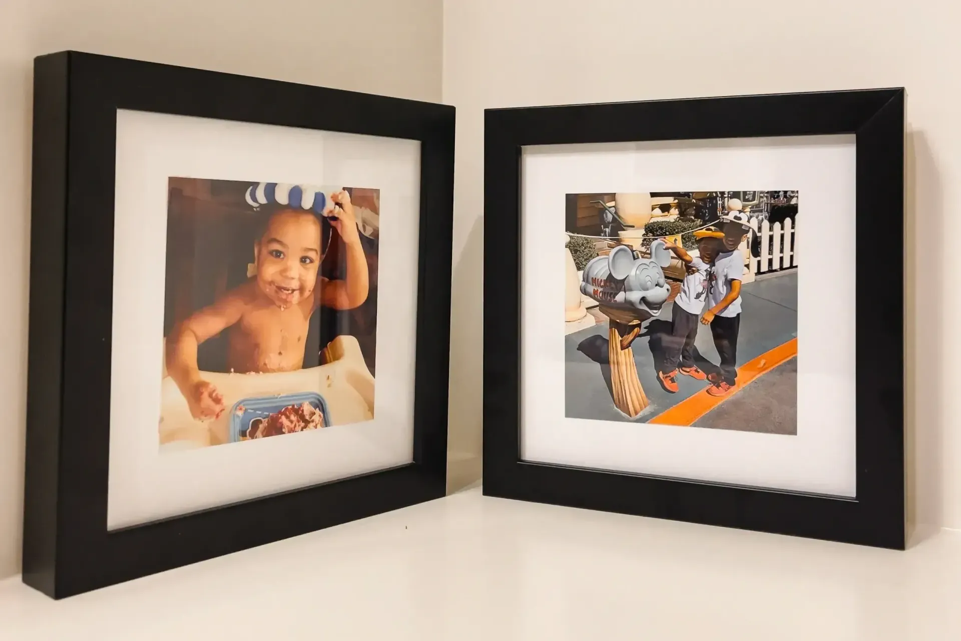 Two black-framed photos on a white wall, one showing a smiling child and the other an abstract collage.