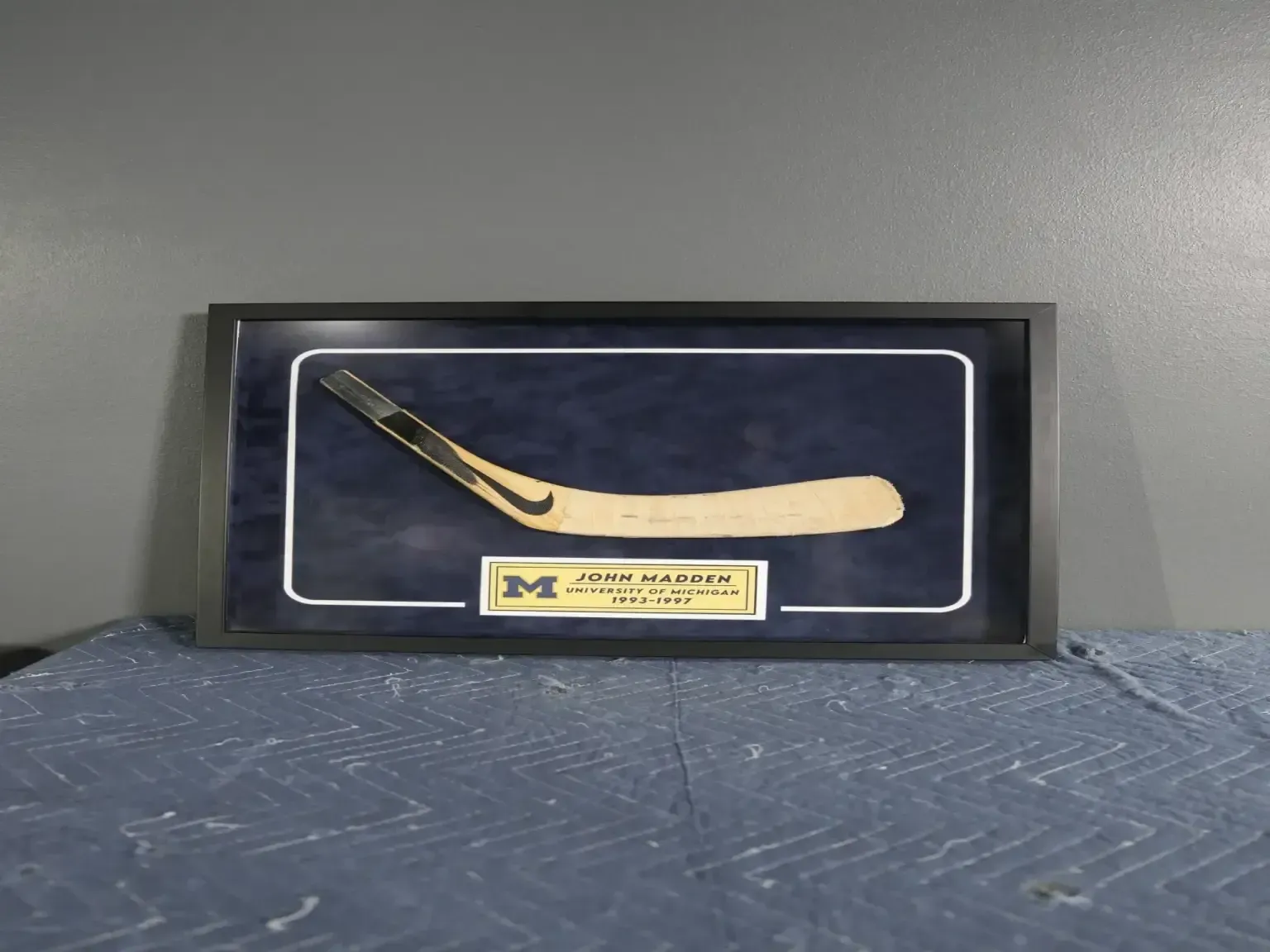 Framed display of a wooden hockey stick on a patterned blue surface