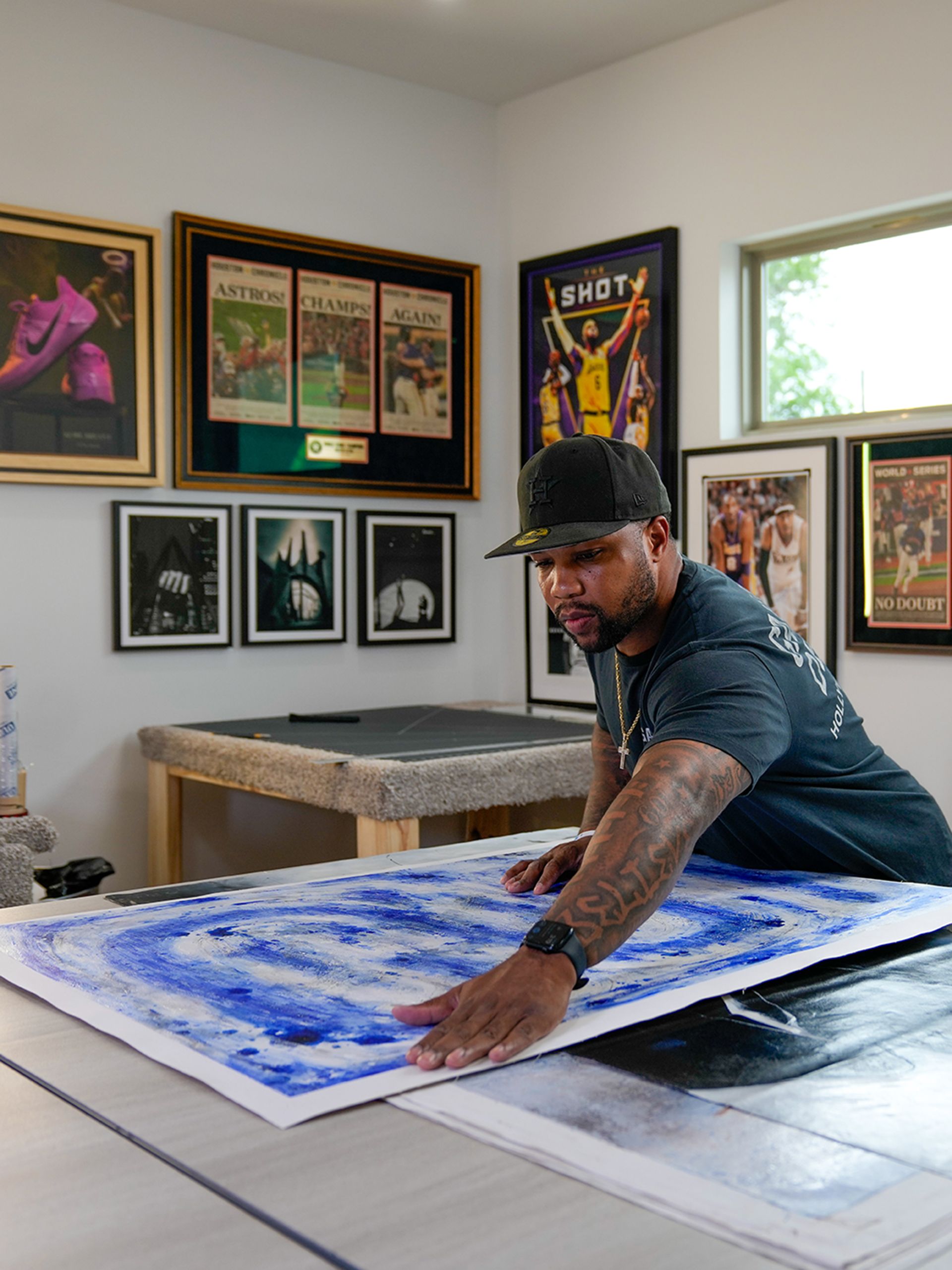 Artist smoothing blue paint on a large canvas in a bright studio with framed artwork on the walls